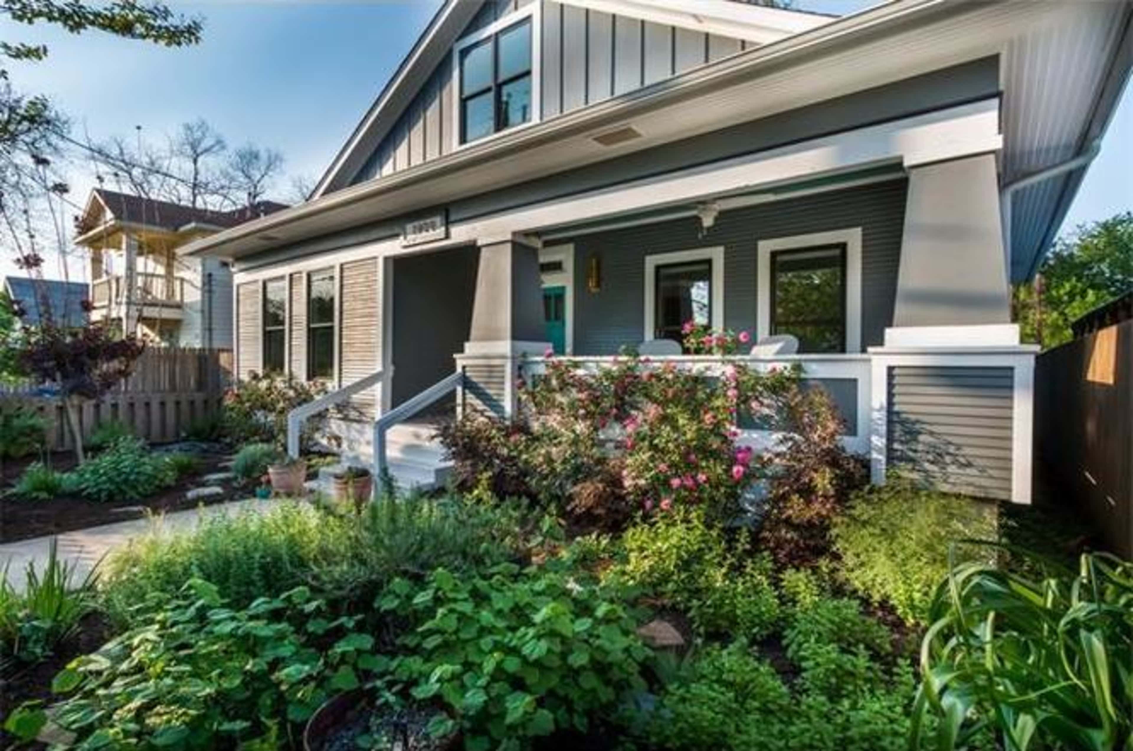 A well-maintained house with a gray exterior and a front porch surrounded by blooming plants and shrubs.