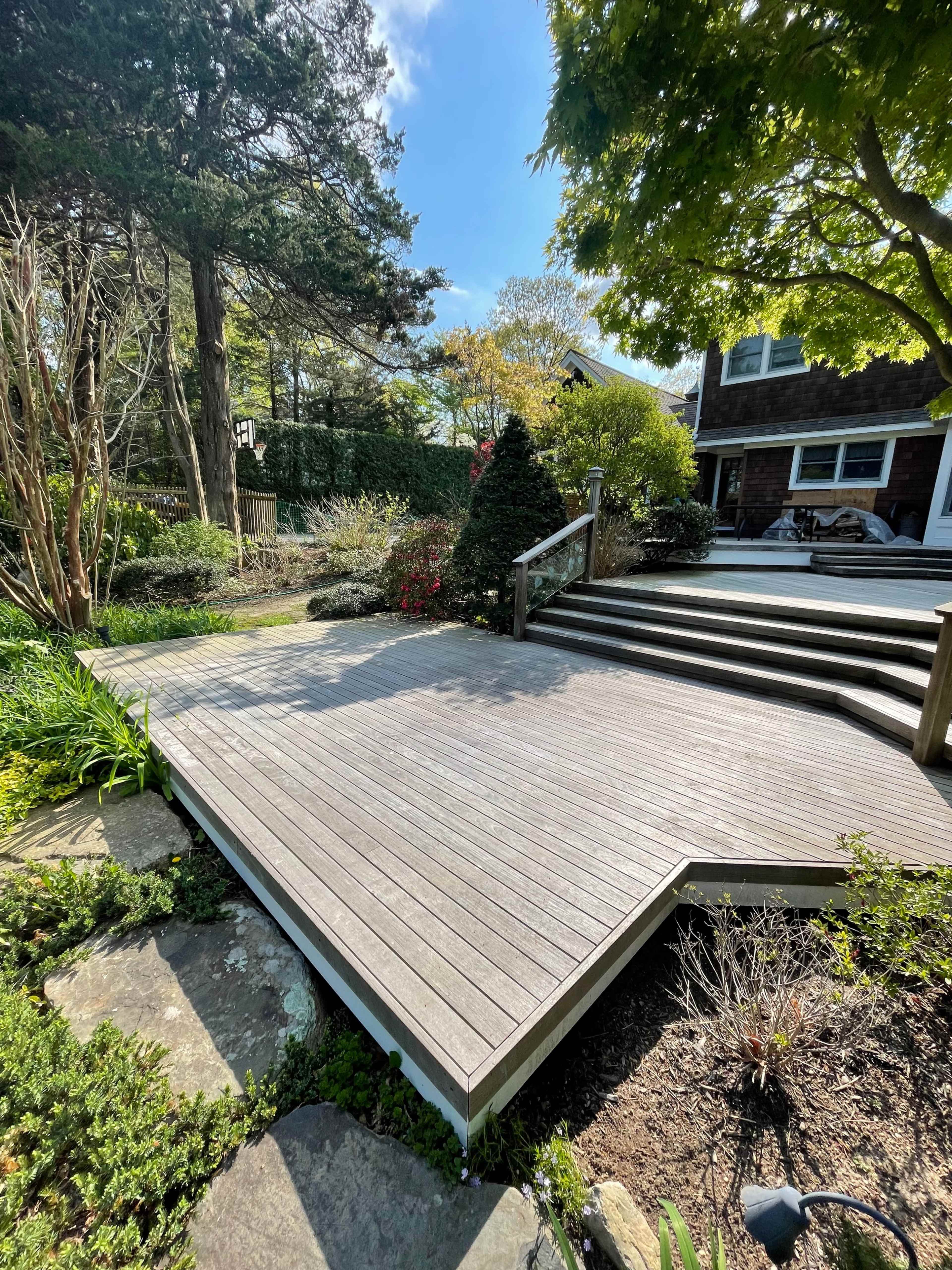 A wooden deck surrounded by landscaped greenery and steps leading up to a house.