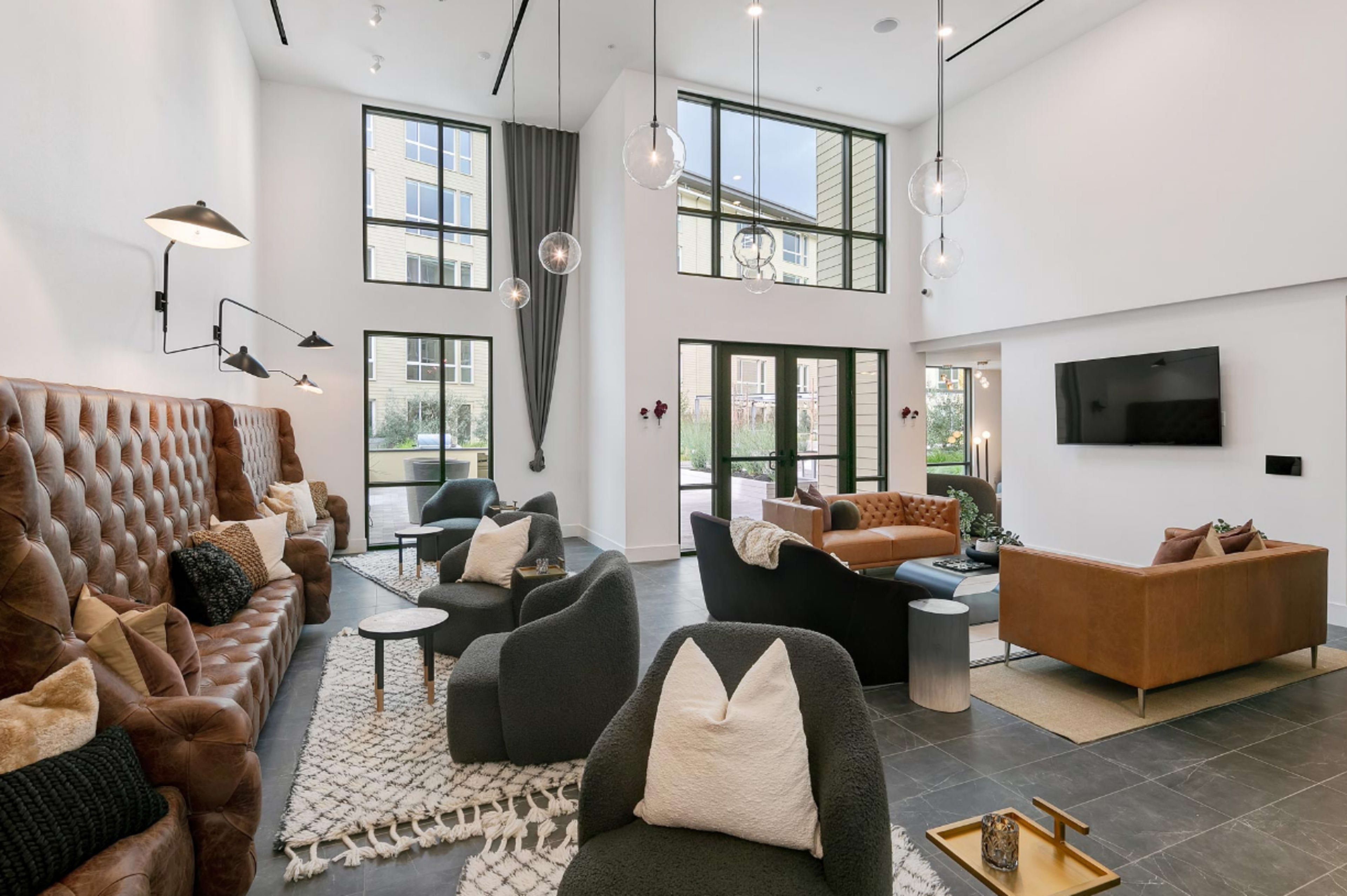 A modern lounge area with large windows, featuring various seating arrangements, decorative pillows, and pendant lighting.