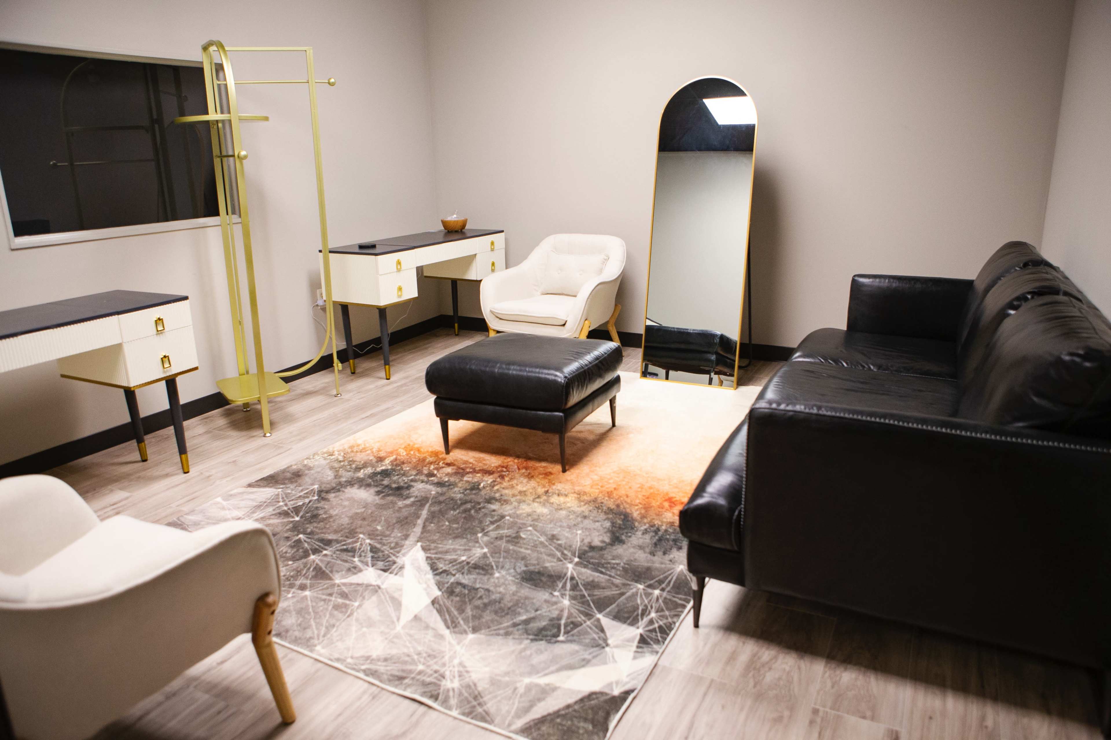 A modern room featuring a black leather sofa, a white armchair, a large mirror, a small coffee table, and a patterned rug.