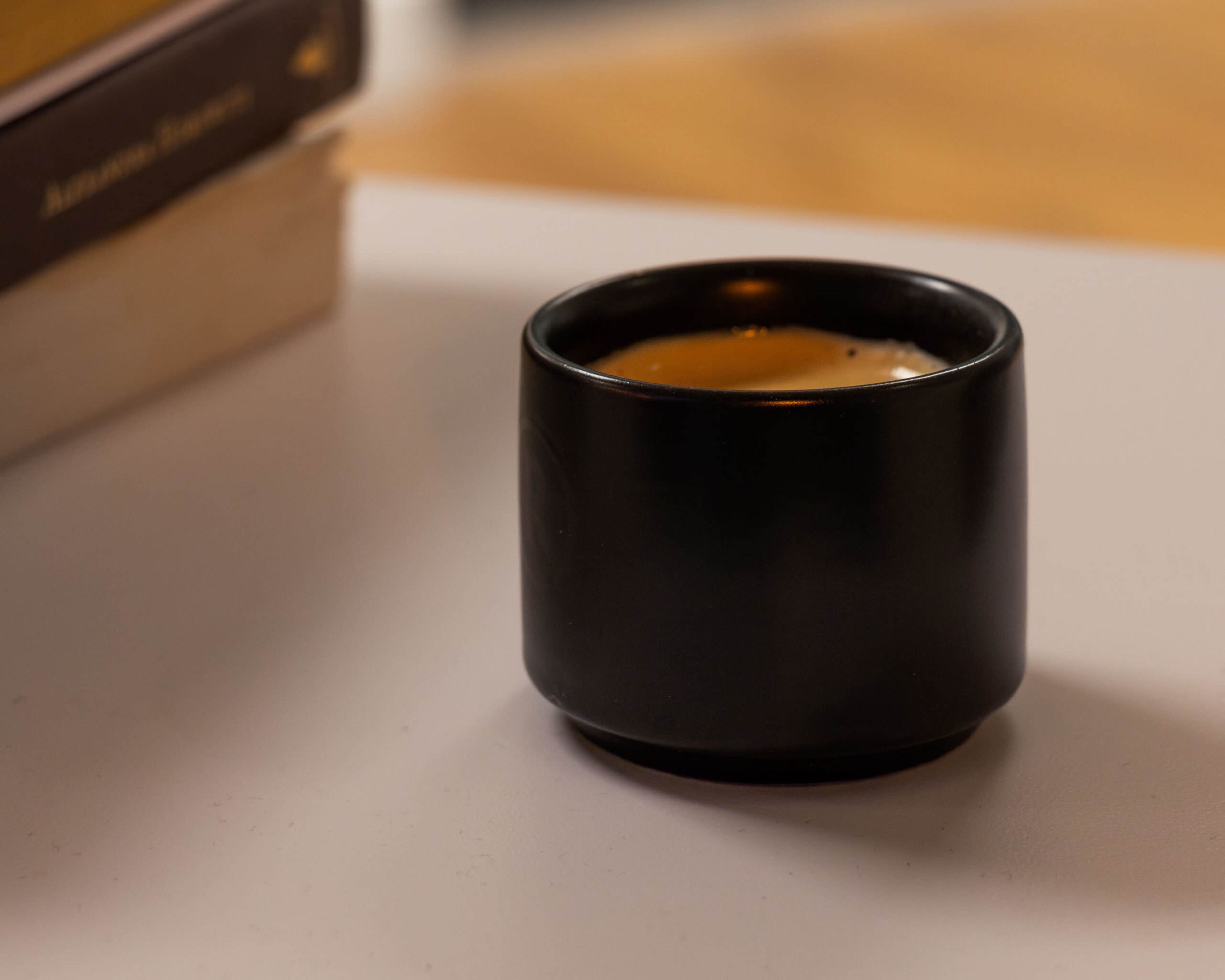 A small black ceramic cup sits on a white surface next to a stack of books.