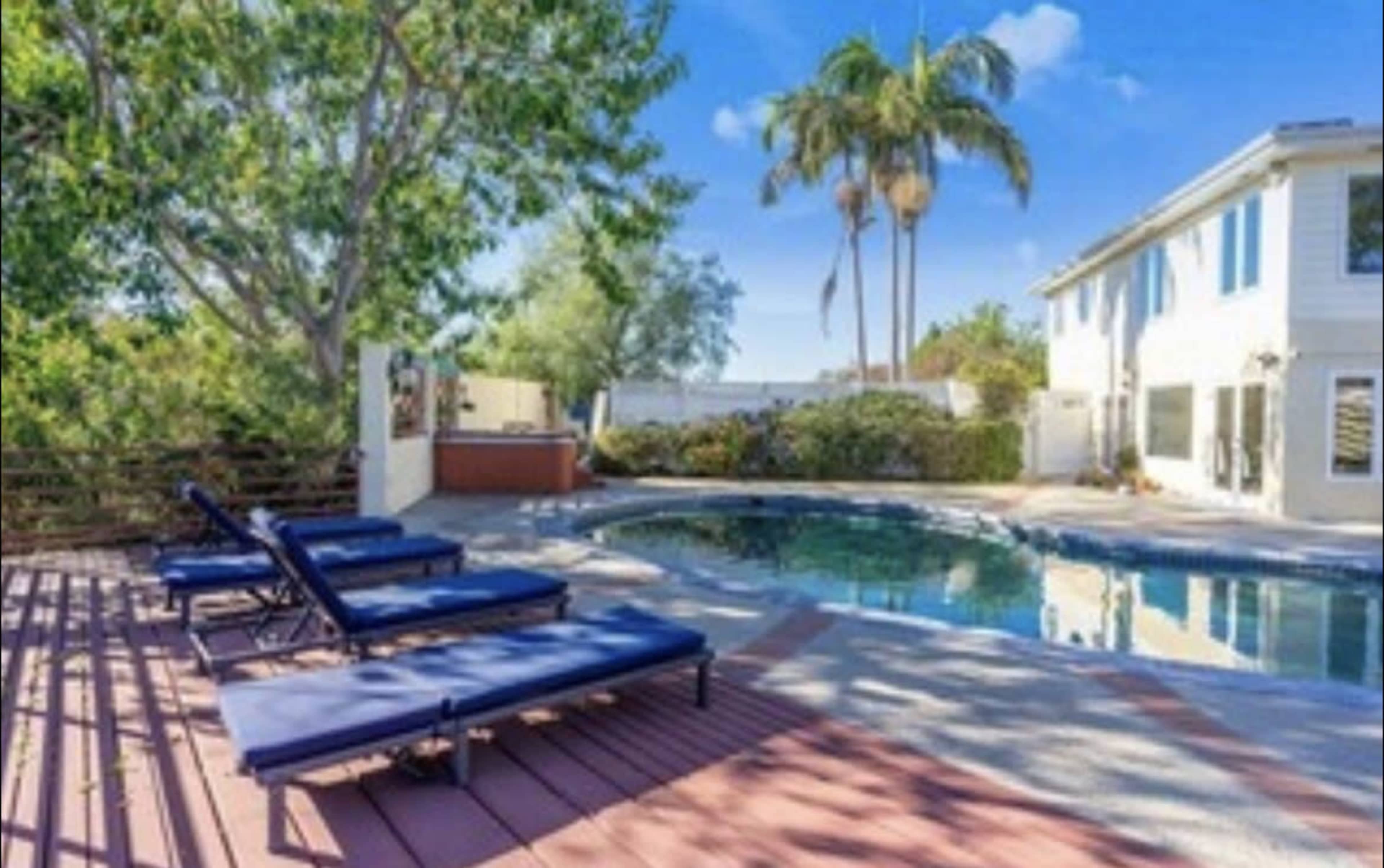 The image shows a quiet backyard with a swimming pool surrounded by lounge chairs and palm trees.