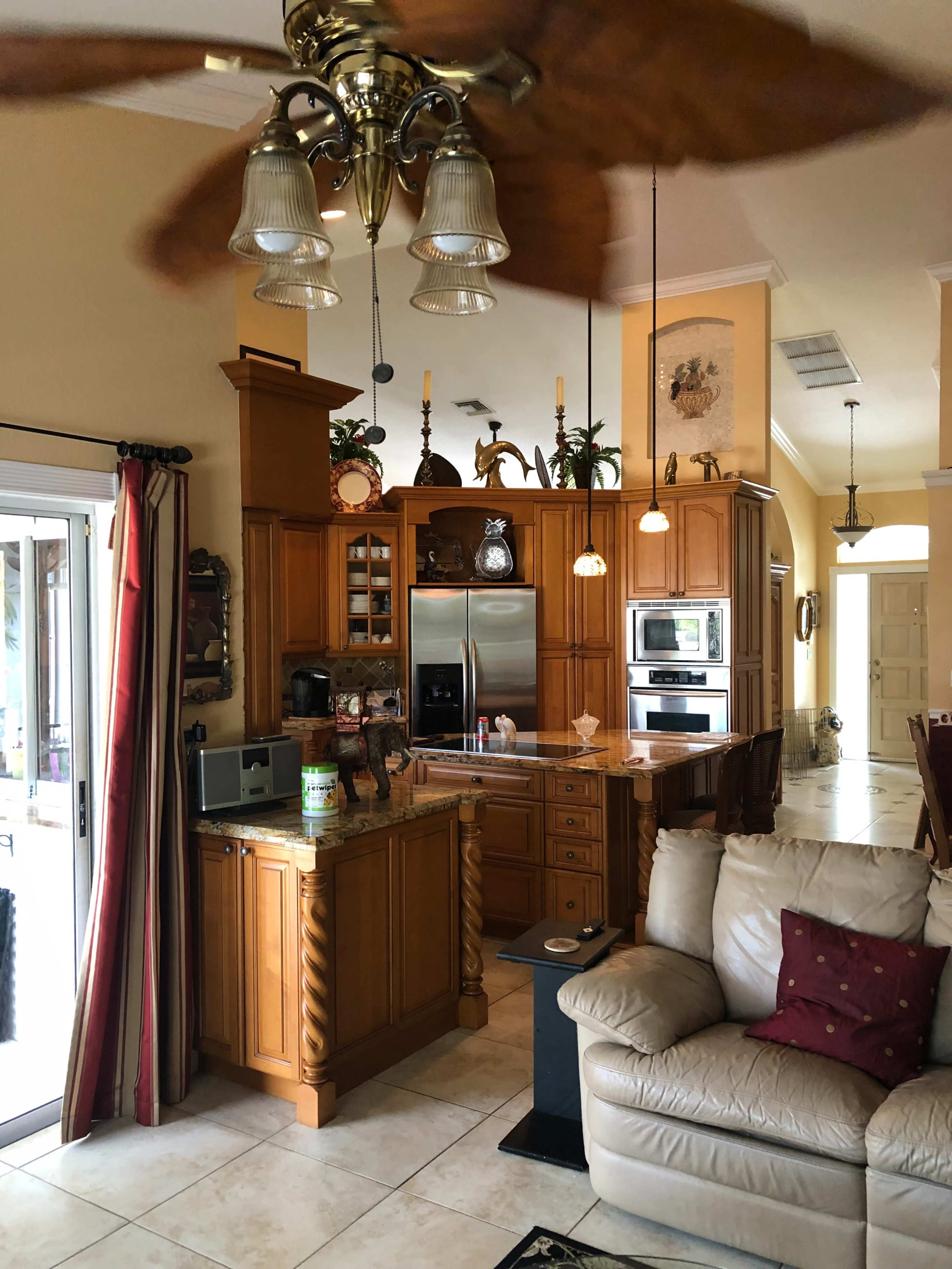A spacious kitchen with wooden cabinetry, modern appliances, and a ceiling fan, adjacent to a living area featuring a light-colored sofa.
