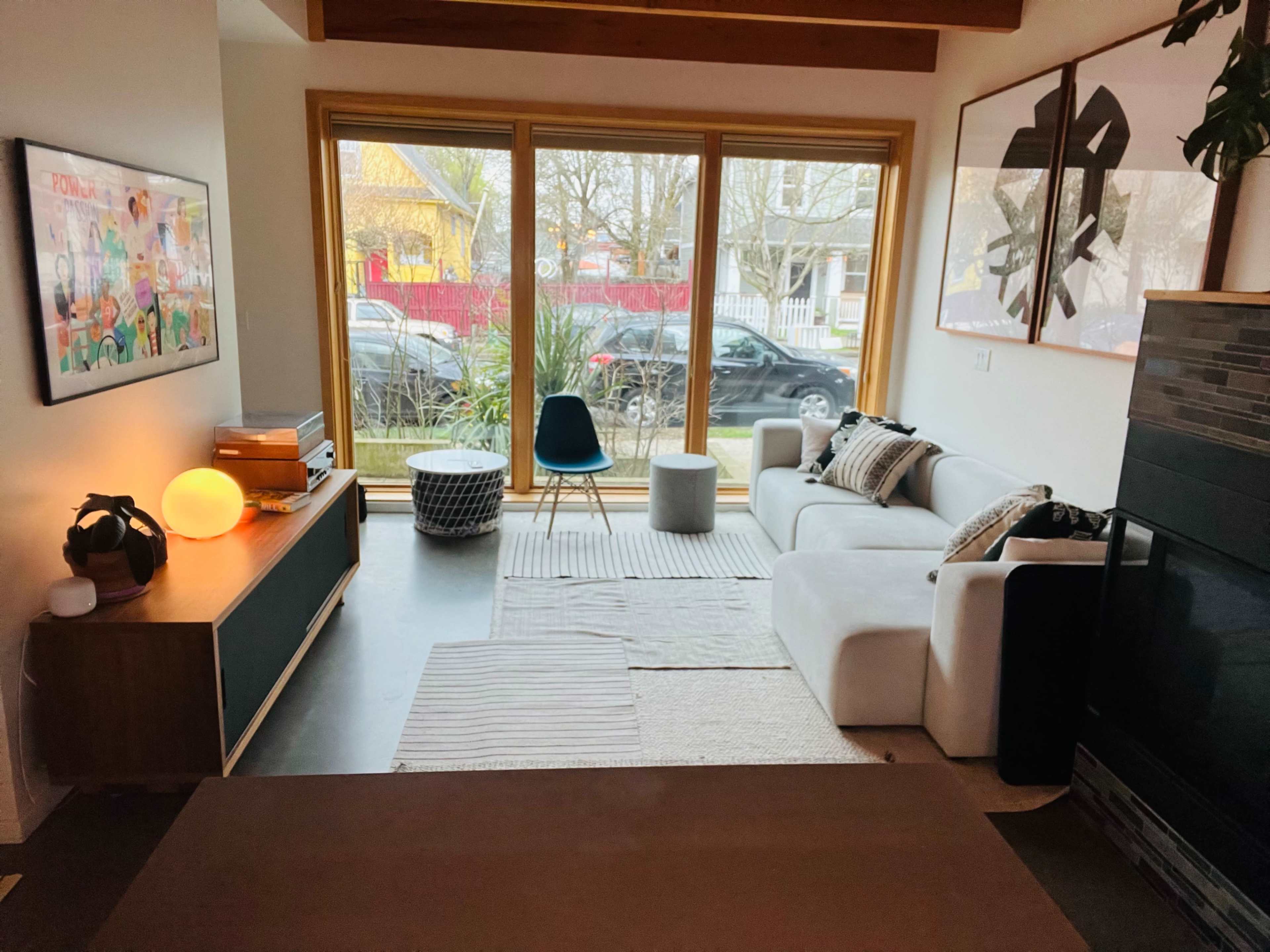 A modern living room features a white sofa, a round chair, and large windows that provide a view of the street outside.