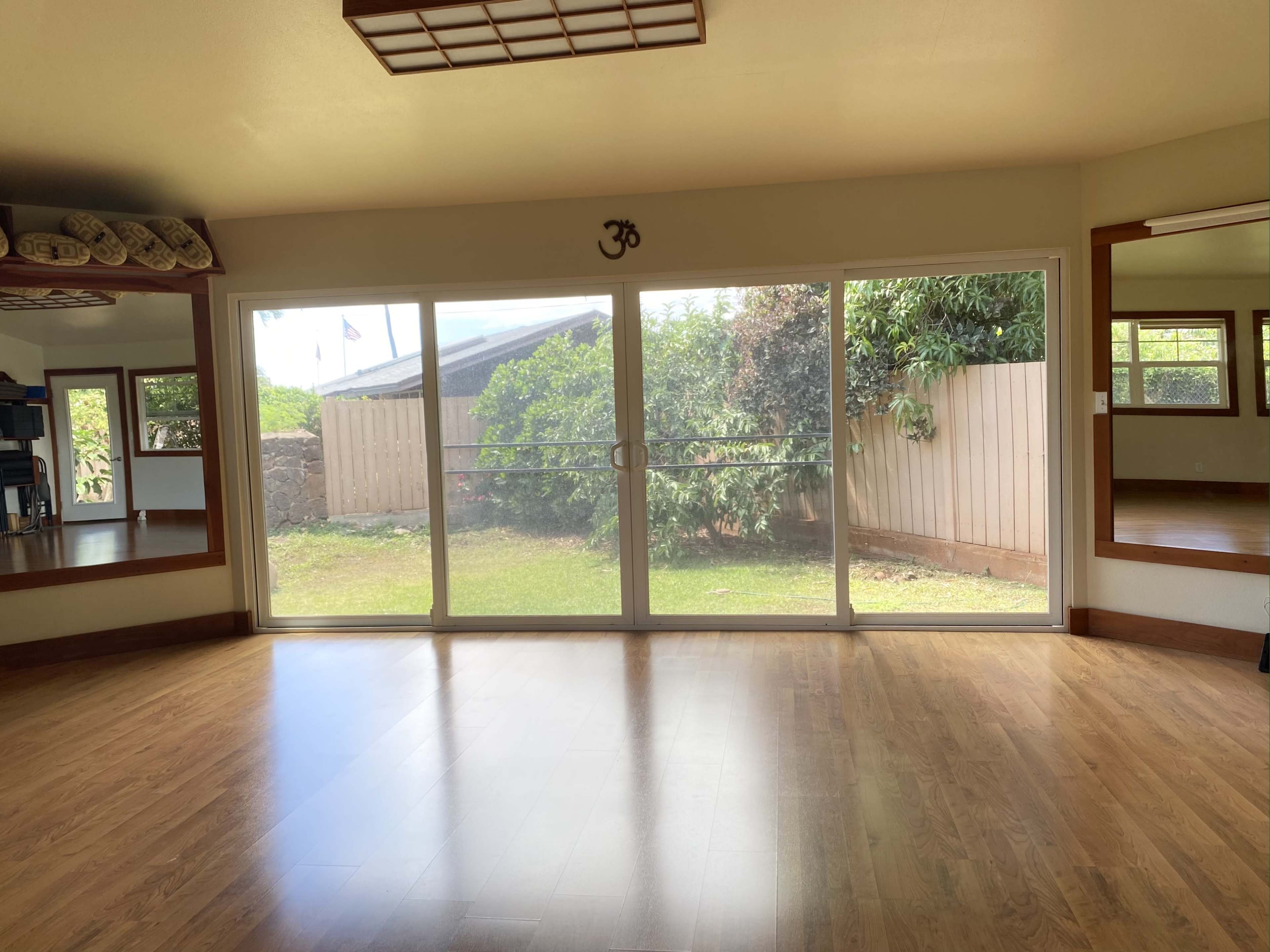 The interior of a room features a large sliding glass door facing a grassy yard with trees, and a wooden floor.