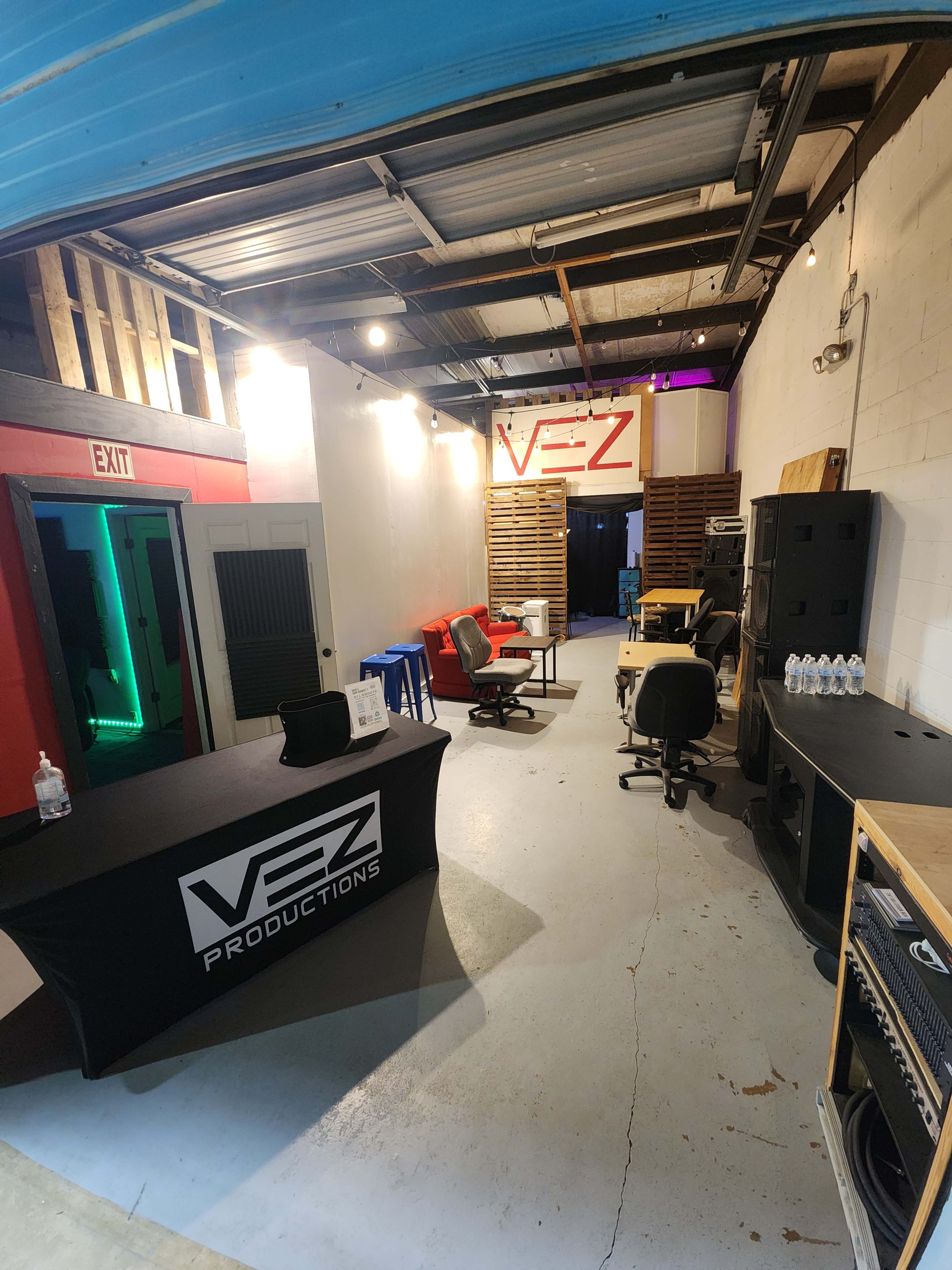 The image shows a production studio interior featuring a reception area with a branded table, seating arrangements, and sound equipment along the walls.