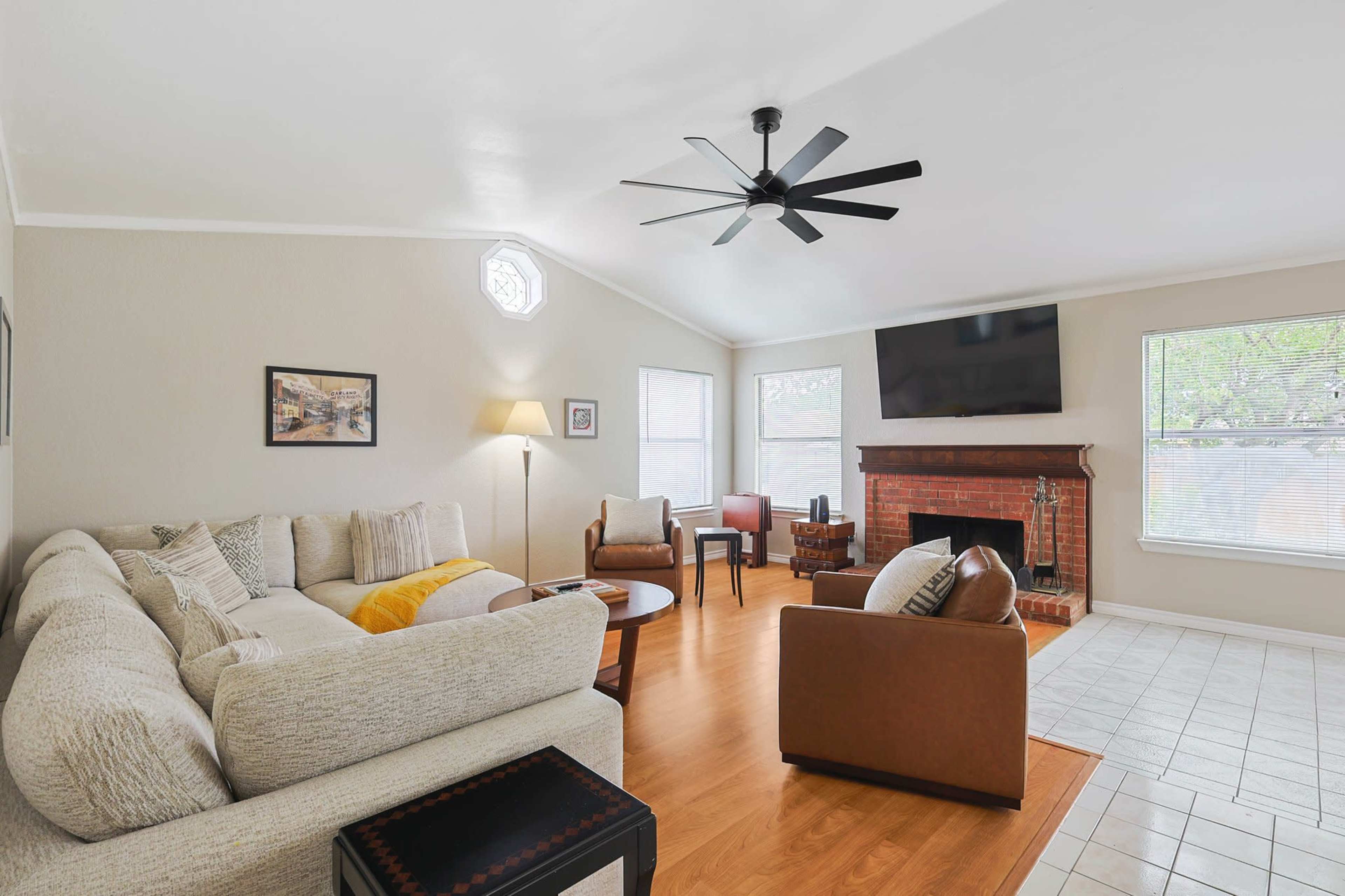 The living room features a sectional sofa, a ceiling fan, a brick fireplace, and a large TV mounted on the wall.