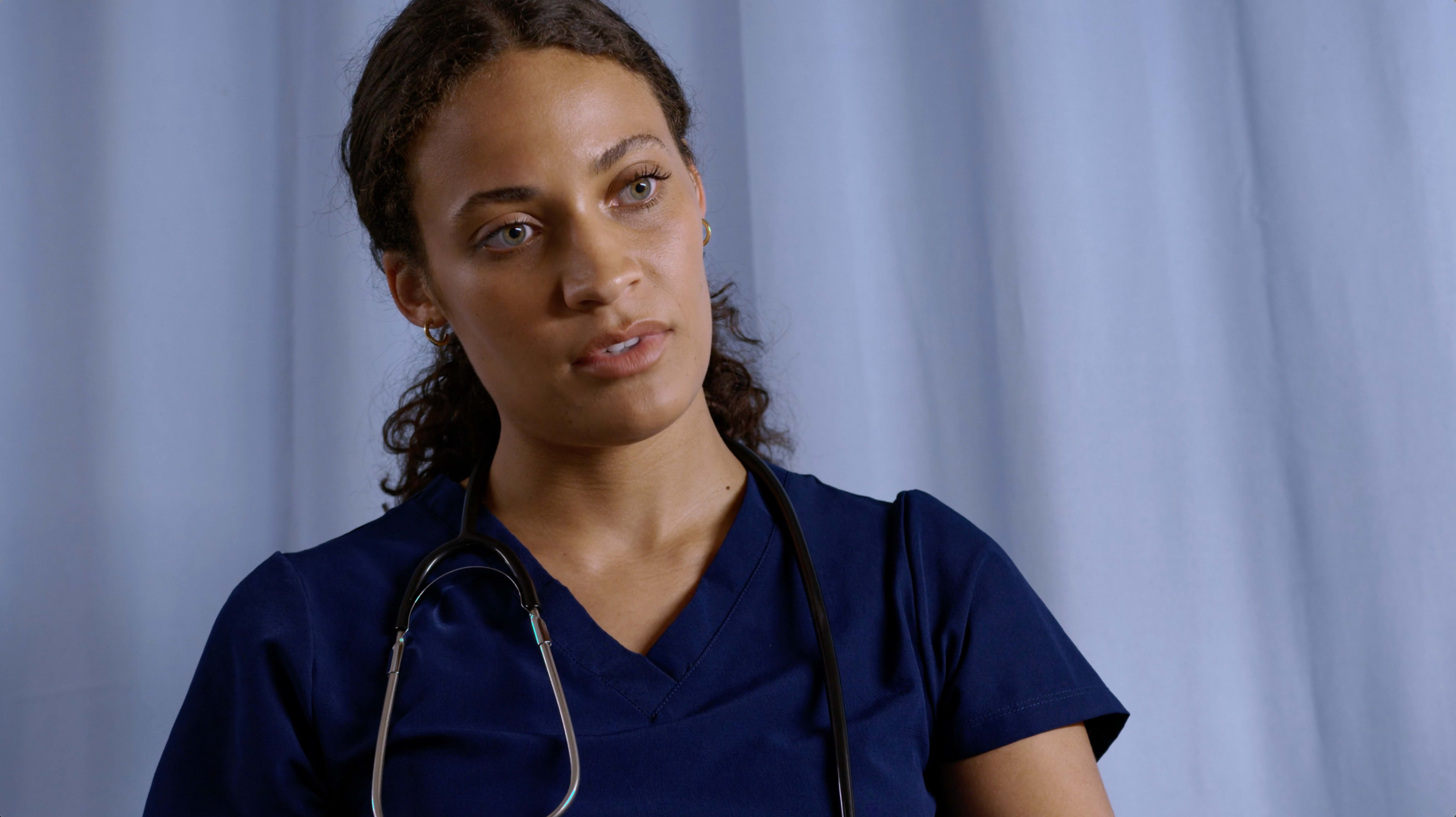 A healthcare professional in blue scrubs with a stethoscope around her neck is listening attentively.