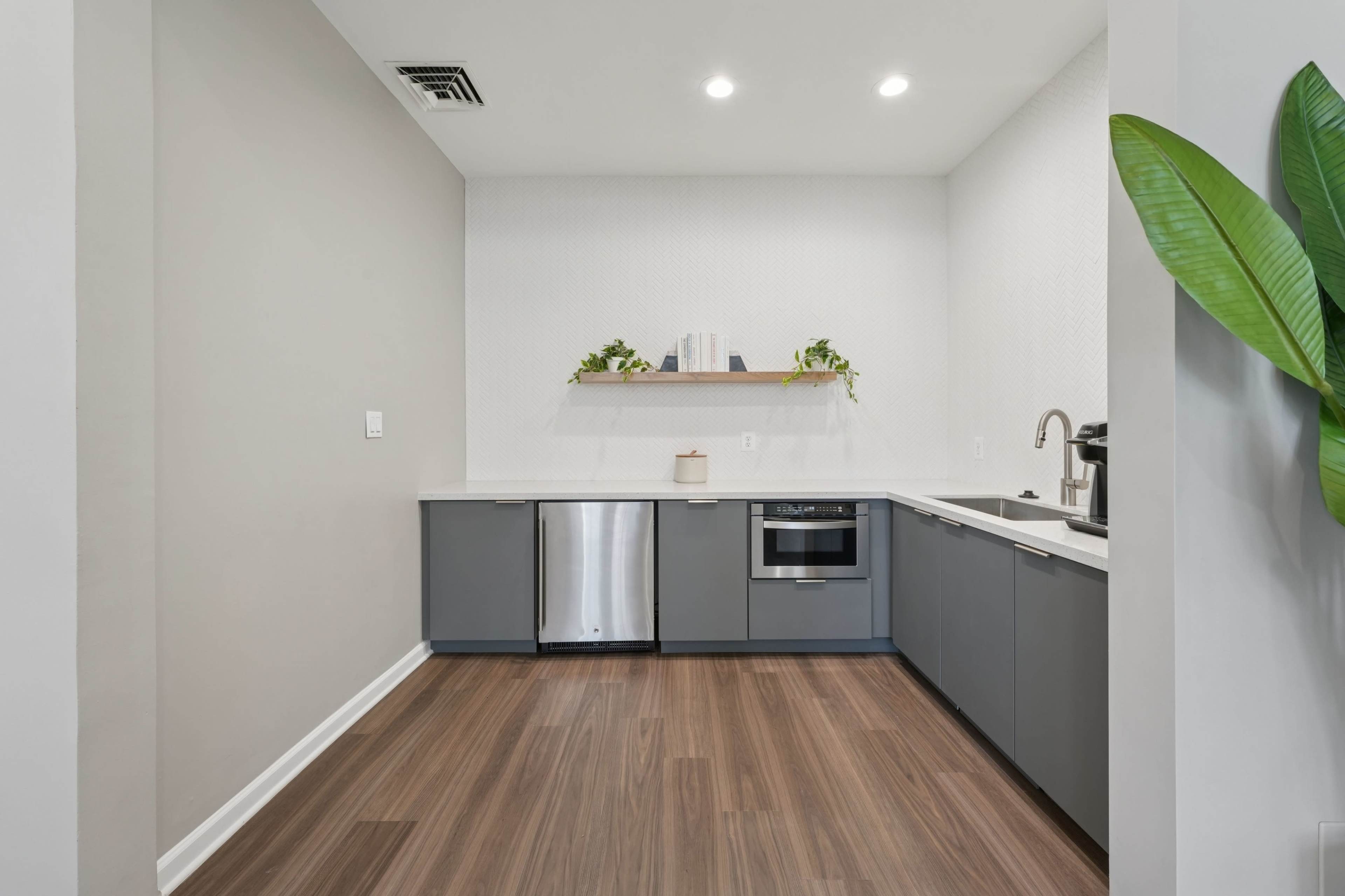 The image shows a modern kitchen with gray cabinets, stainless steel appliances, and a wooden shelf mounted on the wall.