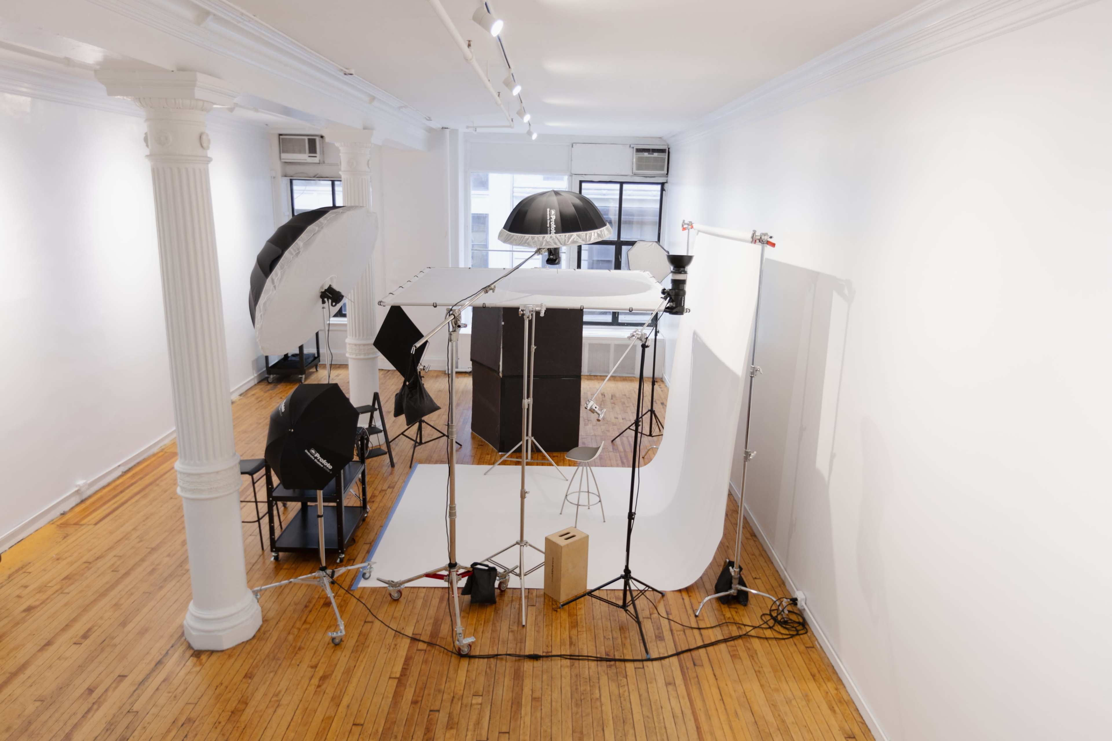 A photography studio setup features various lighting equipment, backdrops, and props arranged in a spacious, well-lit room with wooden floors.
