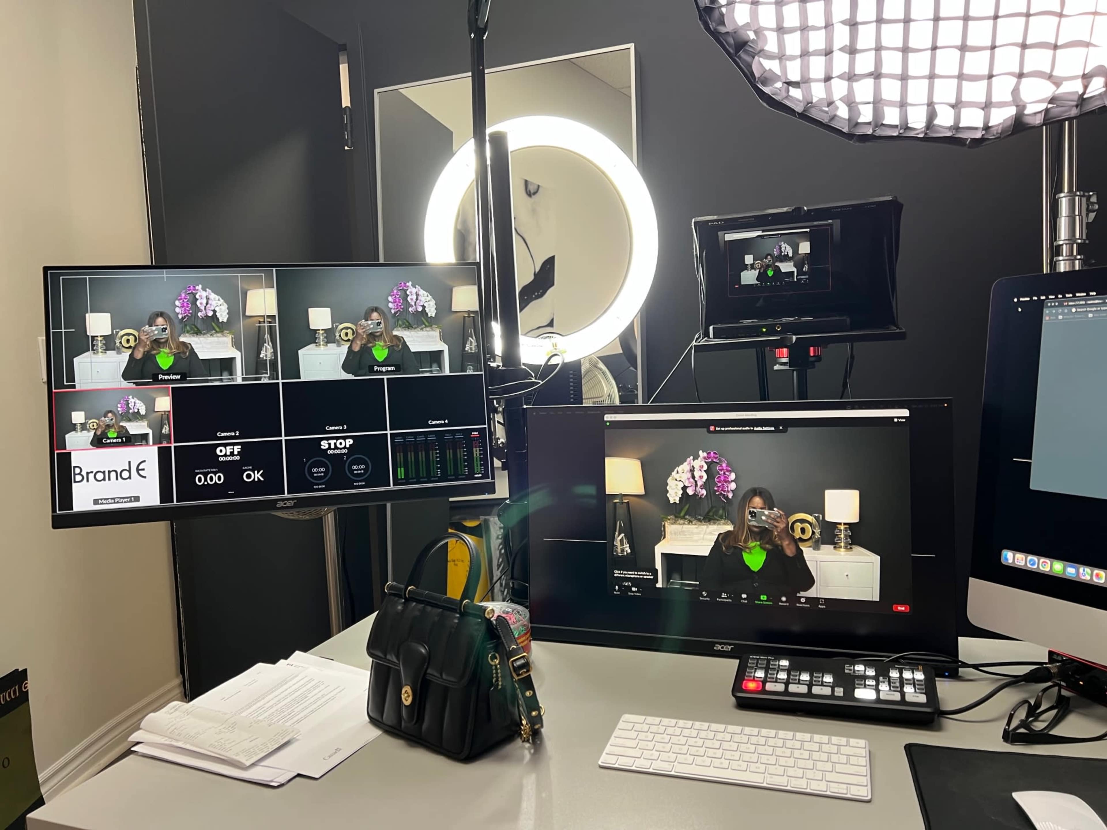 The image shows a video production setup with multiple monitors displaying a live stream, a ring light, and a camera focused on a person sitting at a desk.