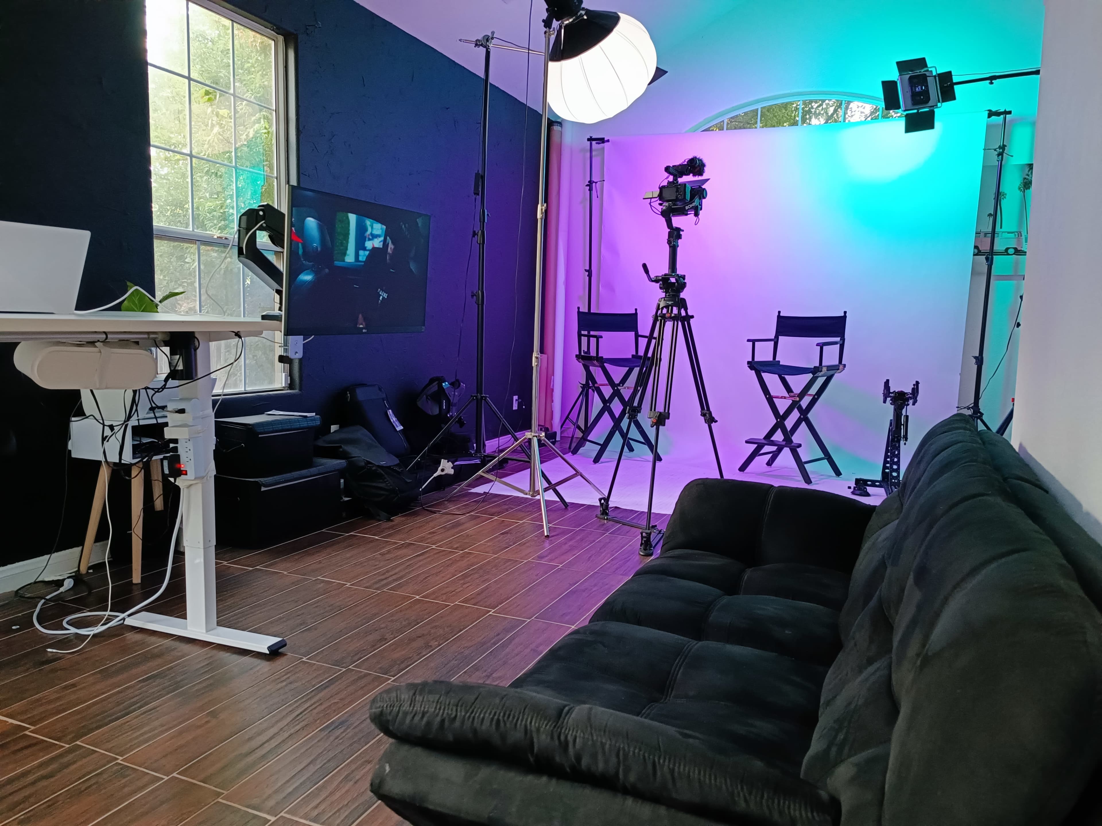 A studio setup with a black couch, two director's chairs, video cameras, and lighting equipment in front of a colorful backdrop.