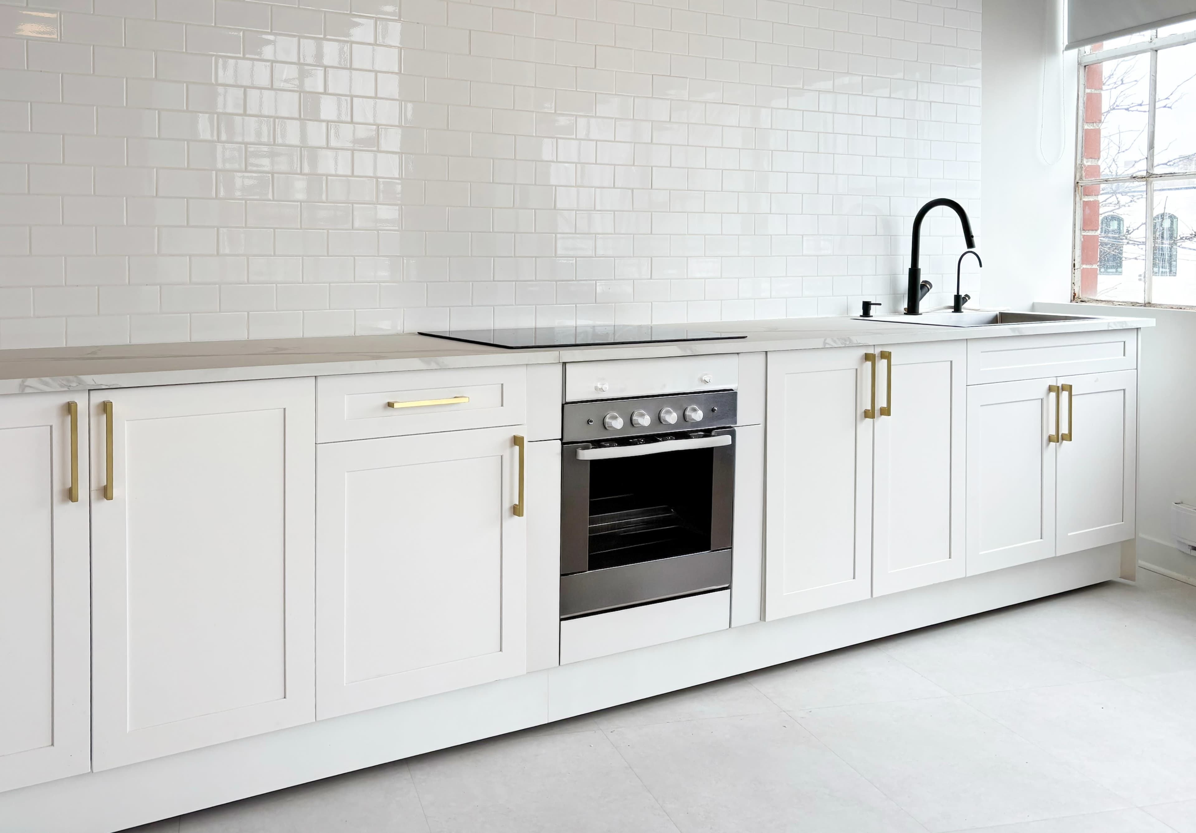 The image shows a modern kitchen with white cabinetry, a sleek black oven, and a minimalist sink with a black faucet.