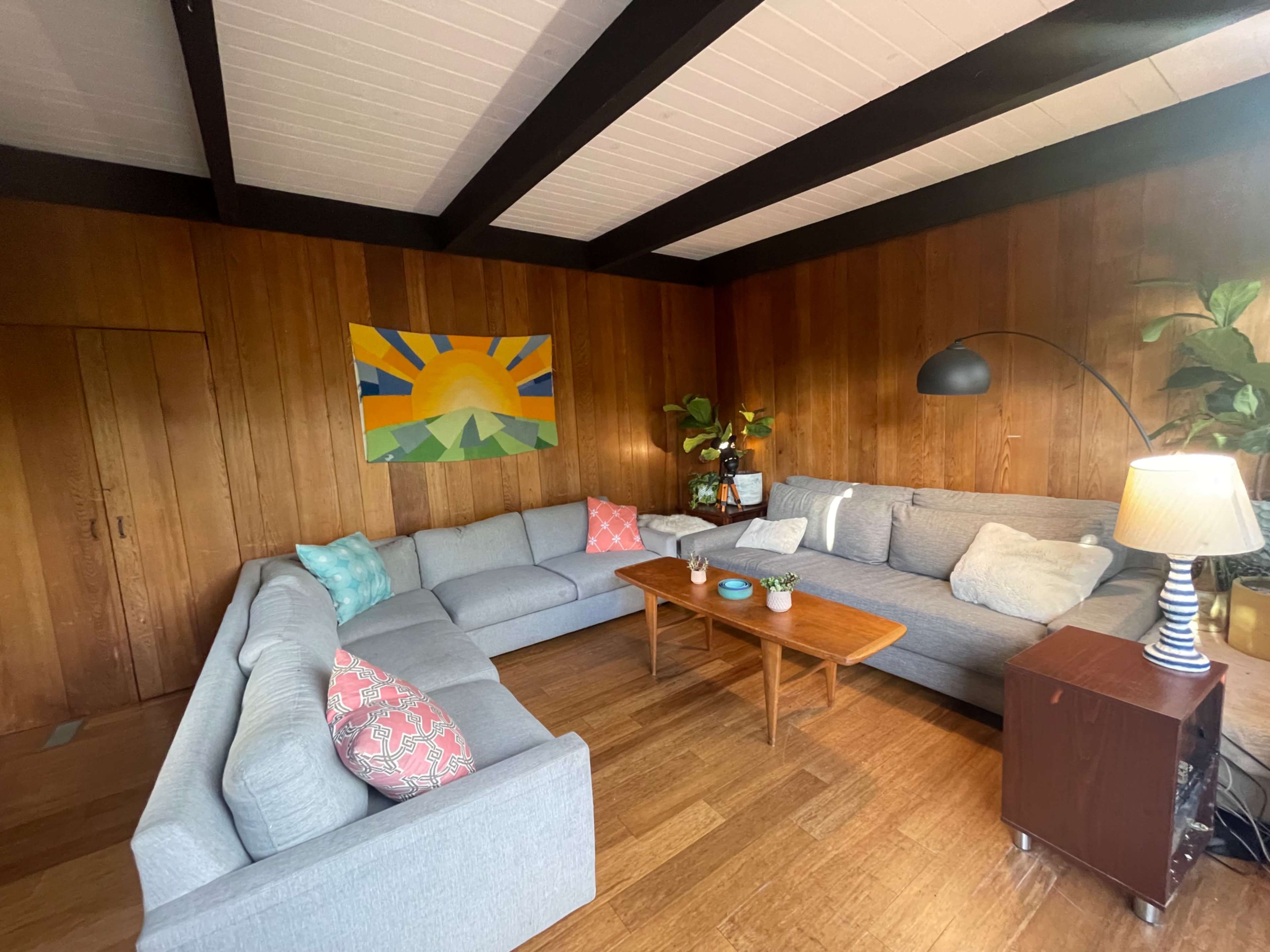 A cozy living room with a large sectional sofa, a wooden table, and a vibrant painting on the wall.