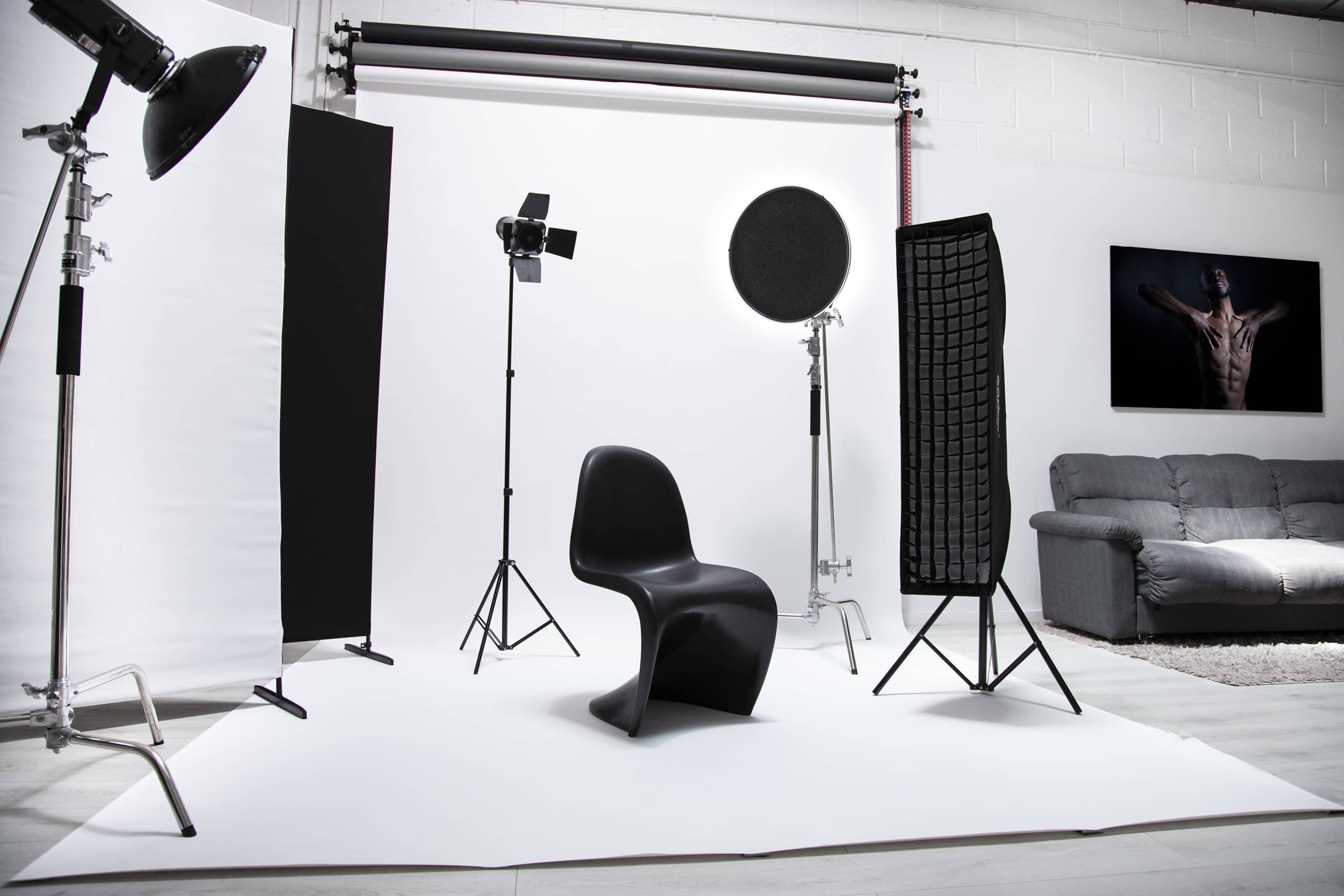 The image shows a photography studio set up with a single black chair in the center, surrounded by lighting equipment and backdrops.
