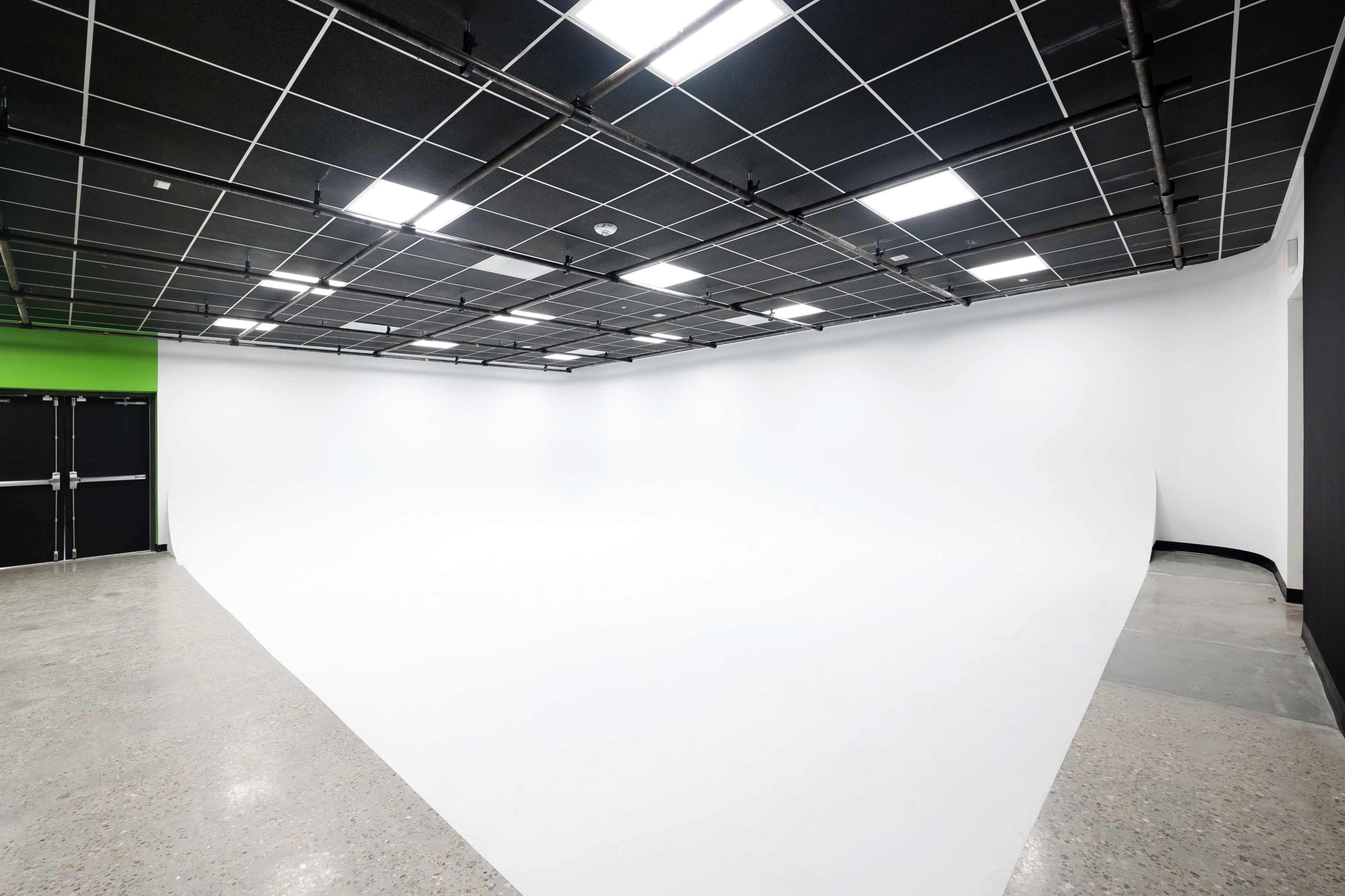 A spacious studio with a seamless white backdrop and a polished concrete floor under overhead fluorescent lighting.