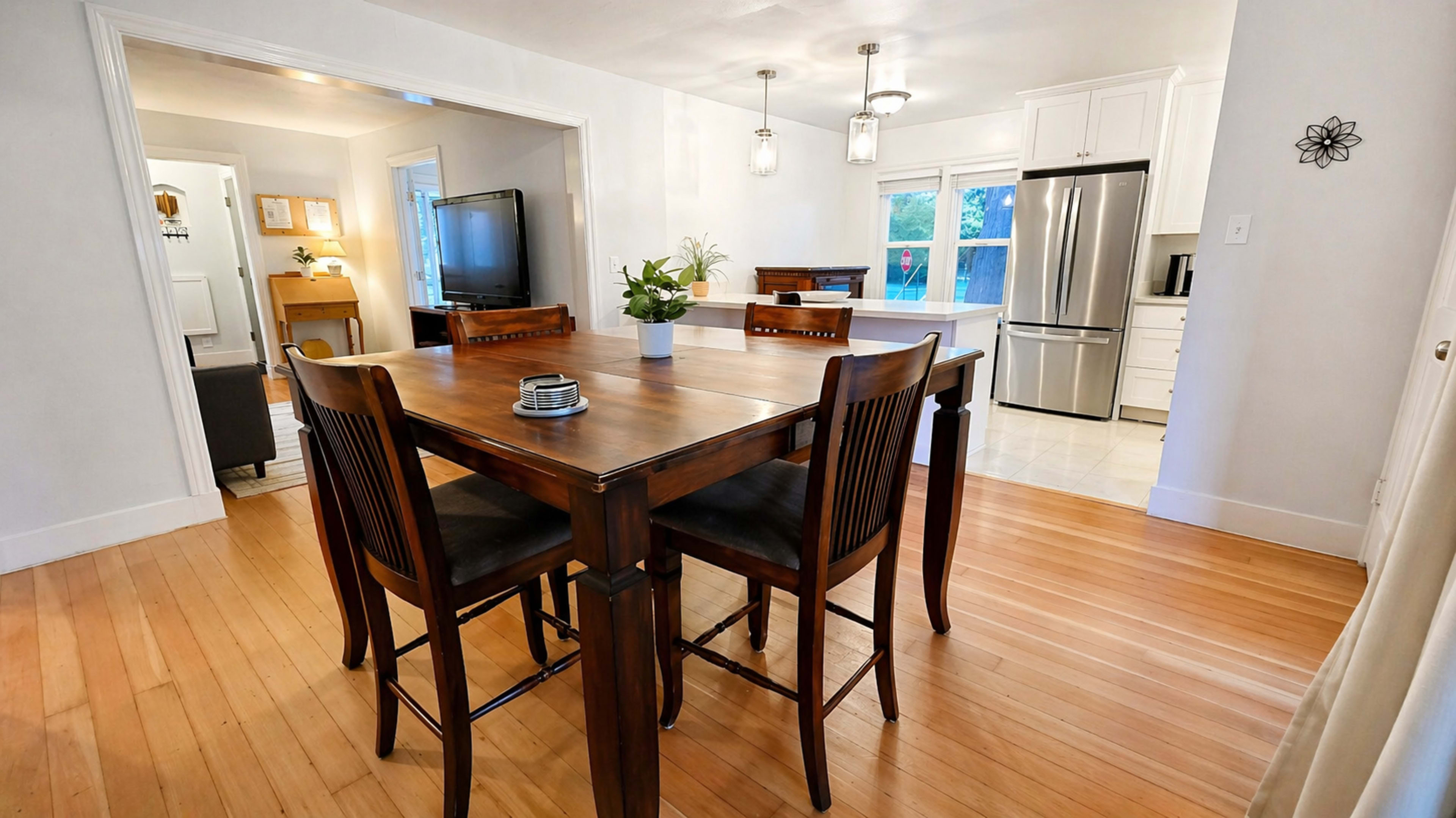 The image shows a dining area with a wooden table and four chairs, leading to a kitchen visible in the background.