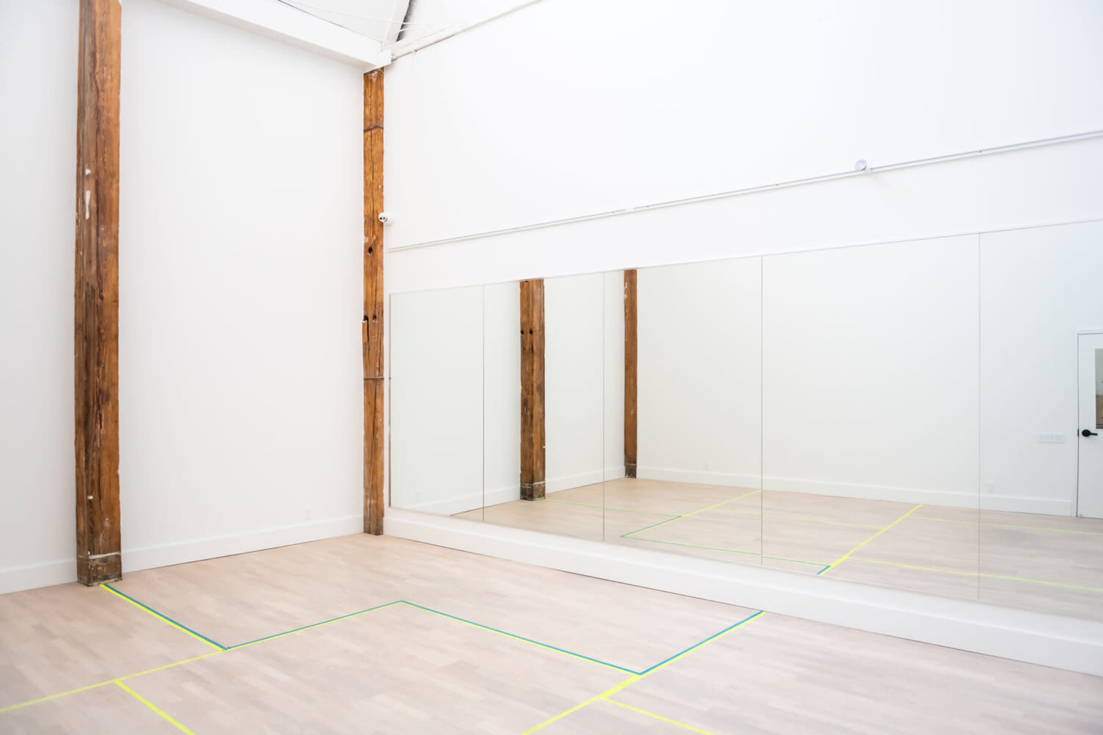 A spacious room with wooden beams, a large mirror on one wall, and marked lines on the floor, indicating a practice or workout area.