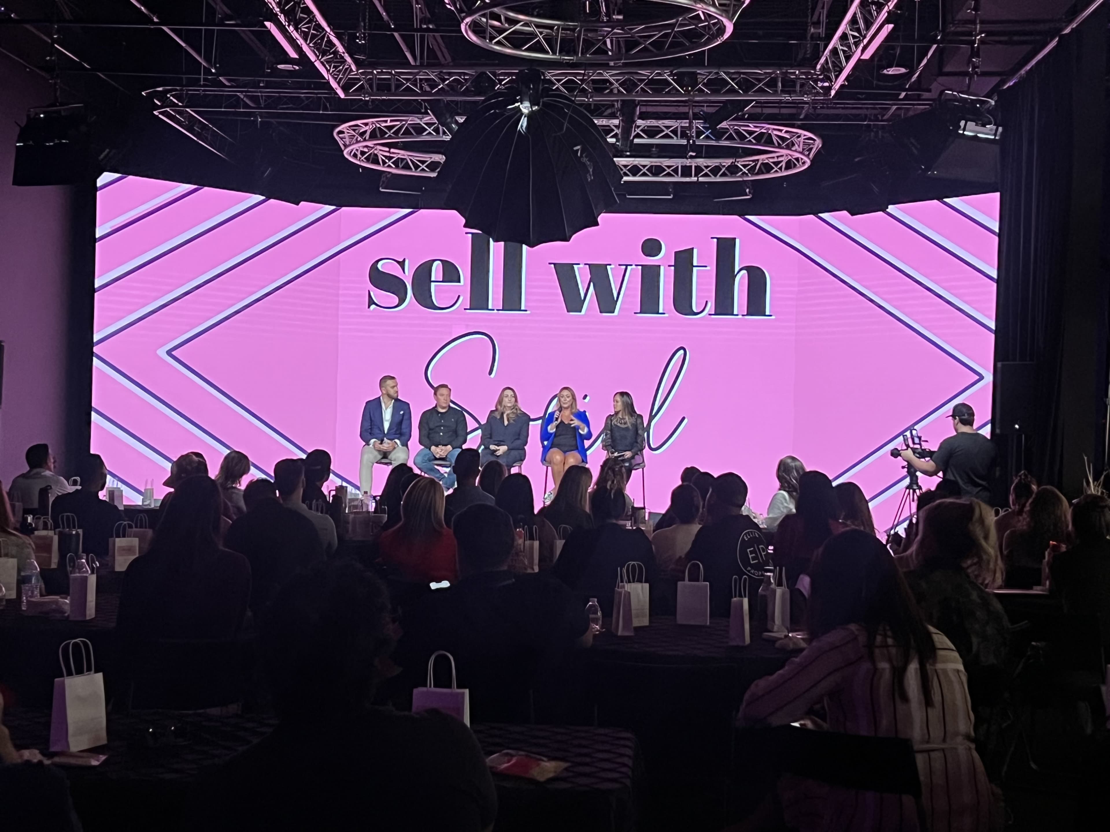 A panel of four speakers is positioned on a stage in front of a large screen displaying the text "sell with Soul," while an audience watches from their seats.
