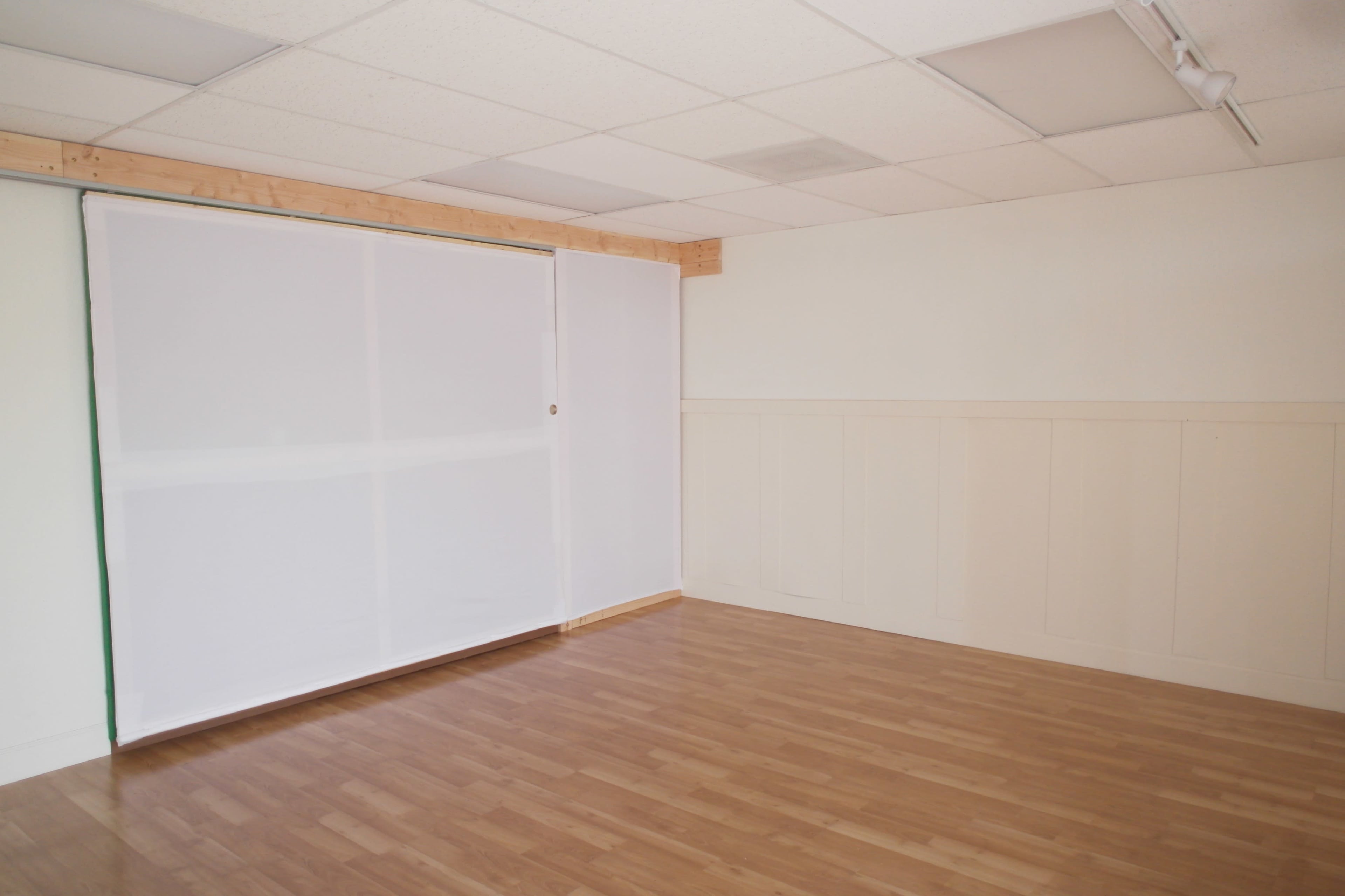 A vacant room with a wooden floor, white walls, and a large, closed white curtain or screen on one side.