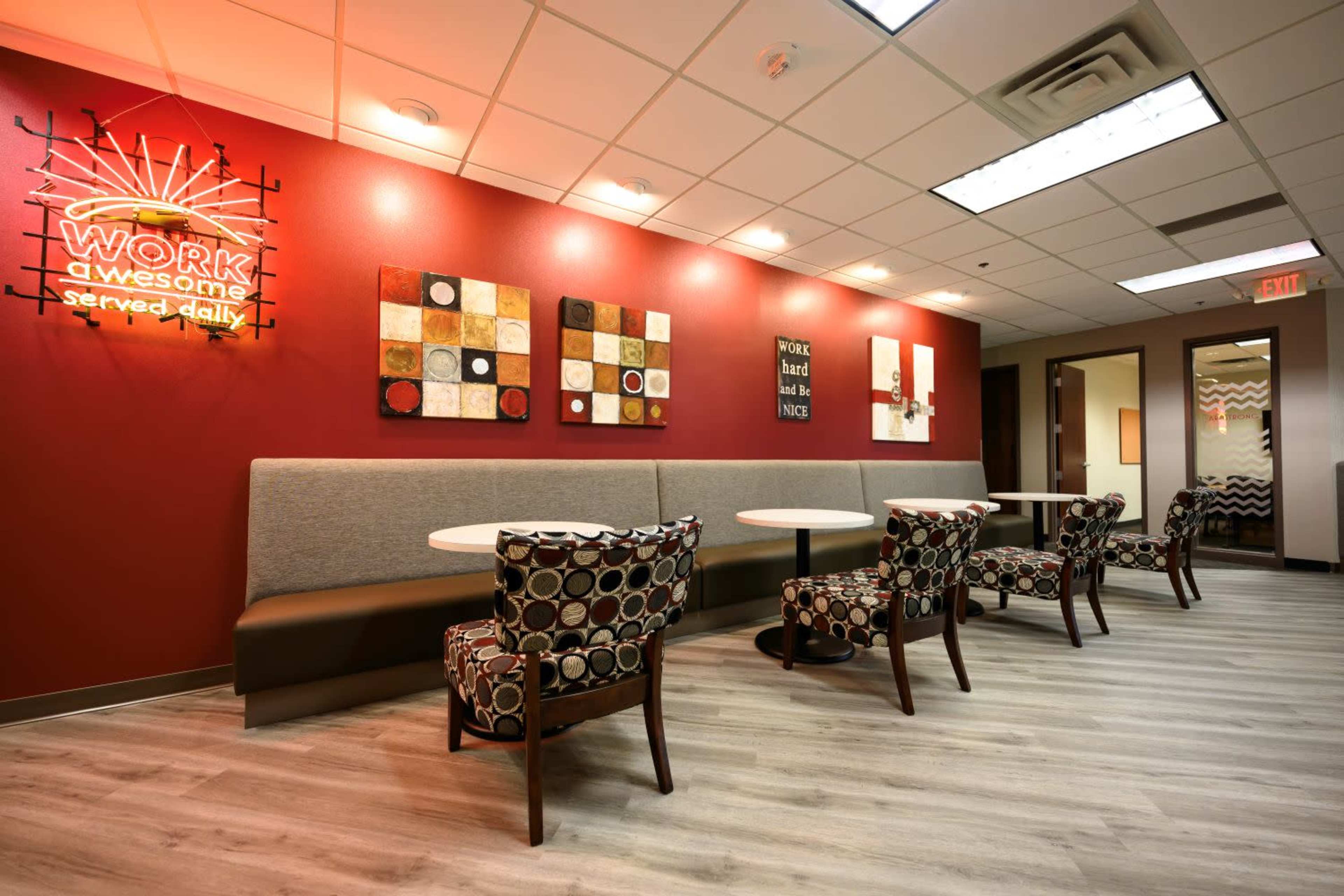 A modern lounge area with patterned chairs and tables arranged against a red wall featuring decorative artwork and neon signs.