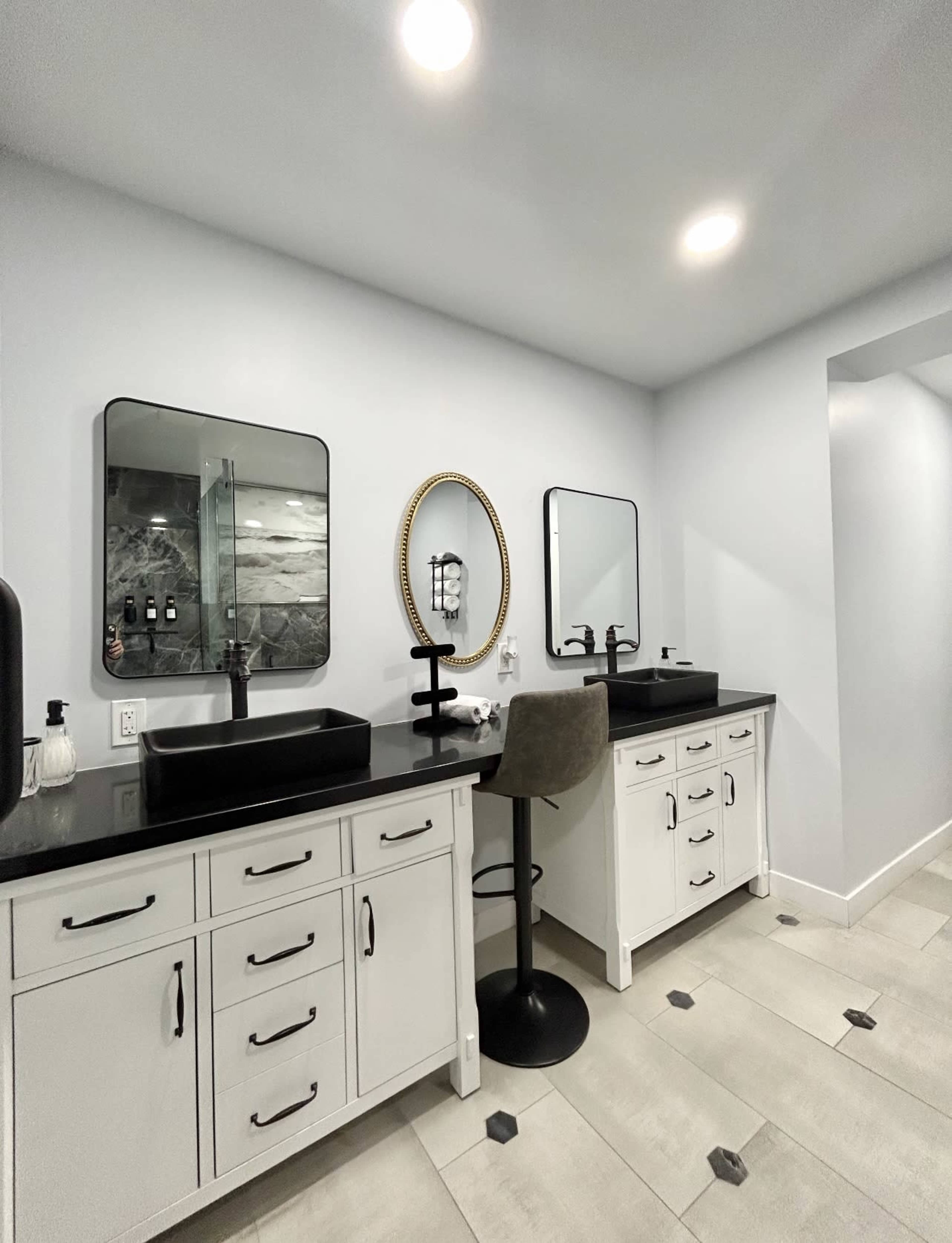 The image shows a modern bathroom with two vanities featuring black sinks, mirrors, and gray tile flooring.