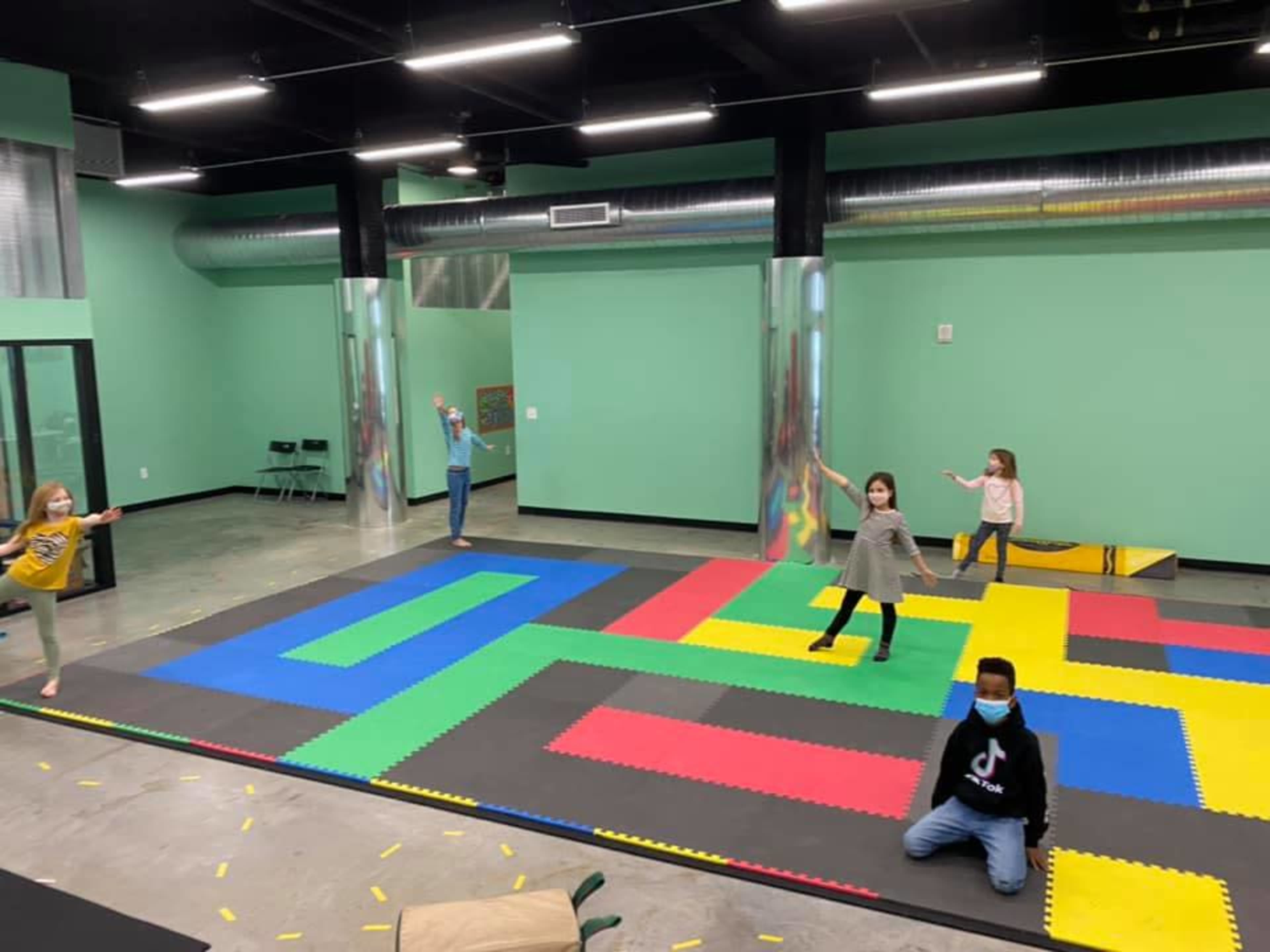 Children are playing in a brightly colored activity space with foam mats and mirrors.
