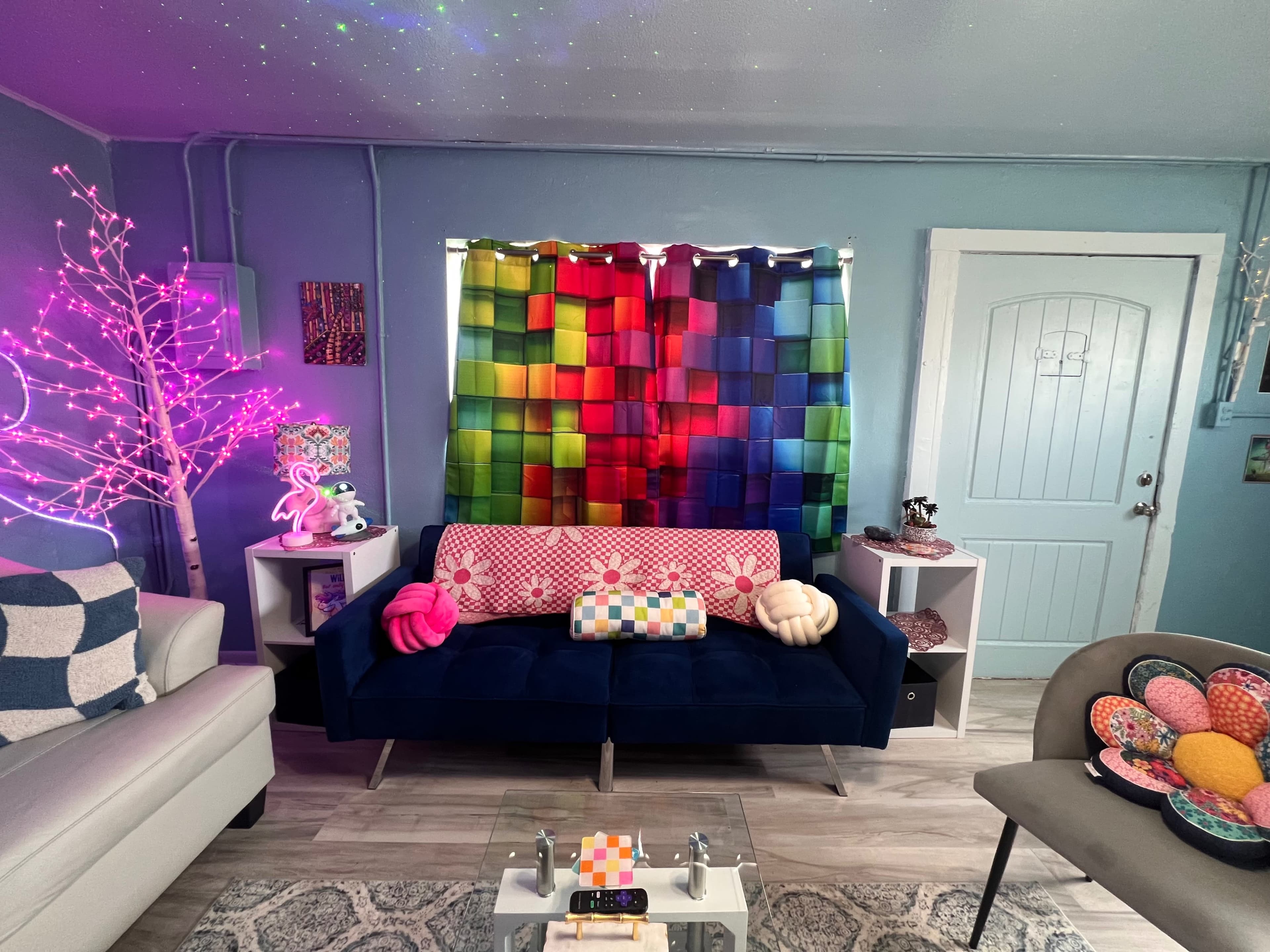A colorful living room features a dark blue sofa, vibrant curtains, and decorative lighting alongside various cushions and a coffee table.