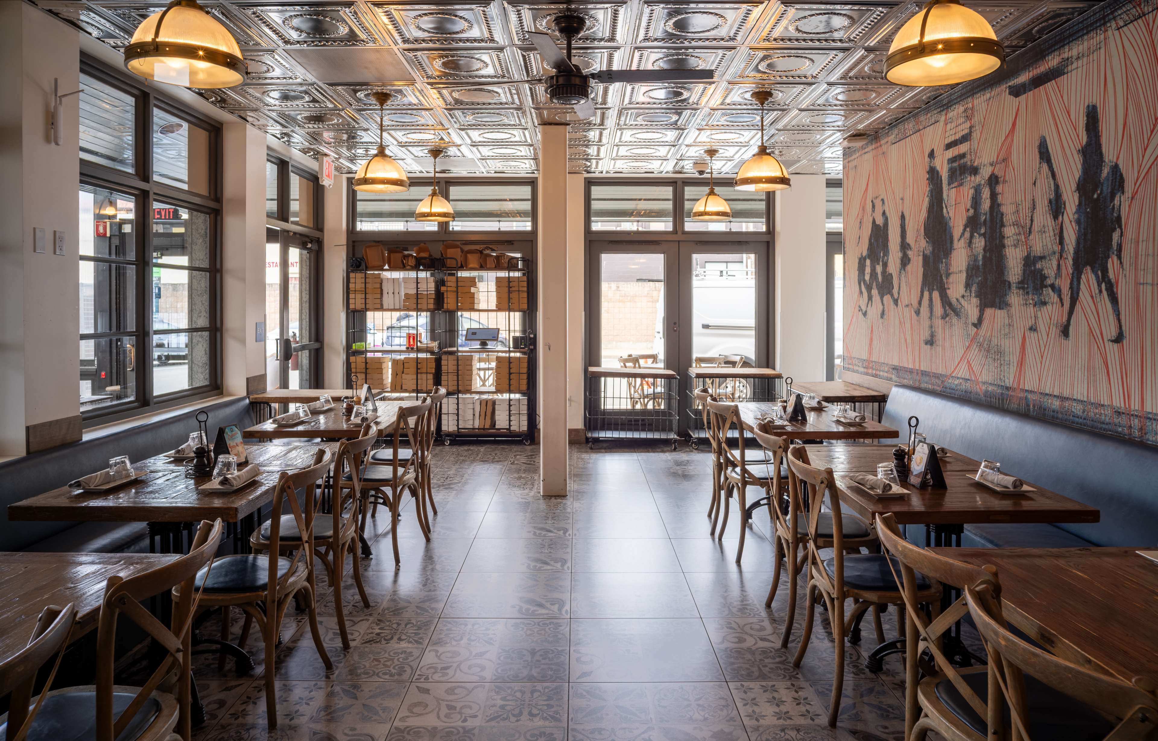 The image shows a modern restaurant interior with wooden tables and chairs, large windows, and a decorative mural on one wall.