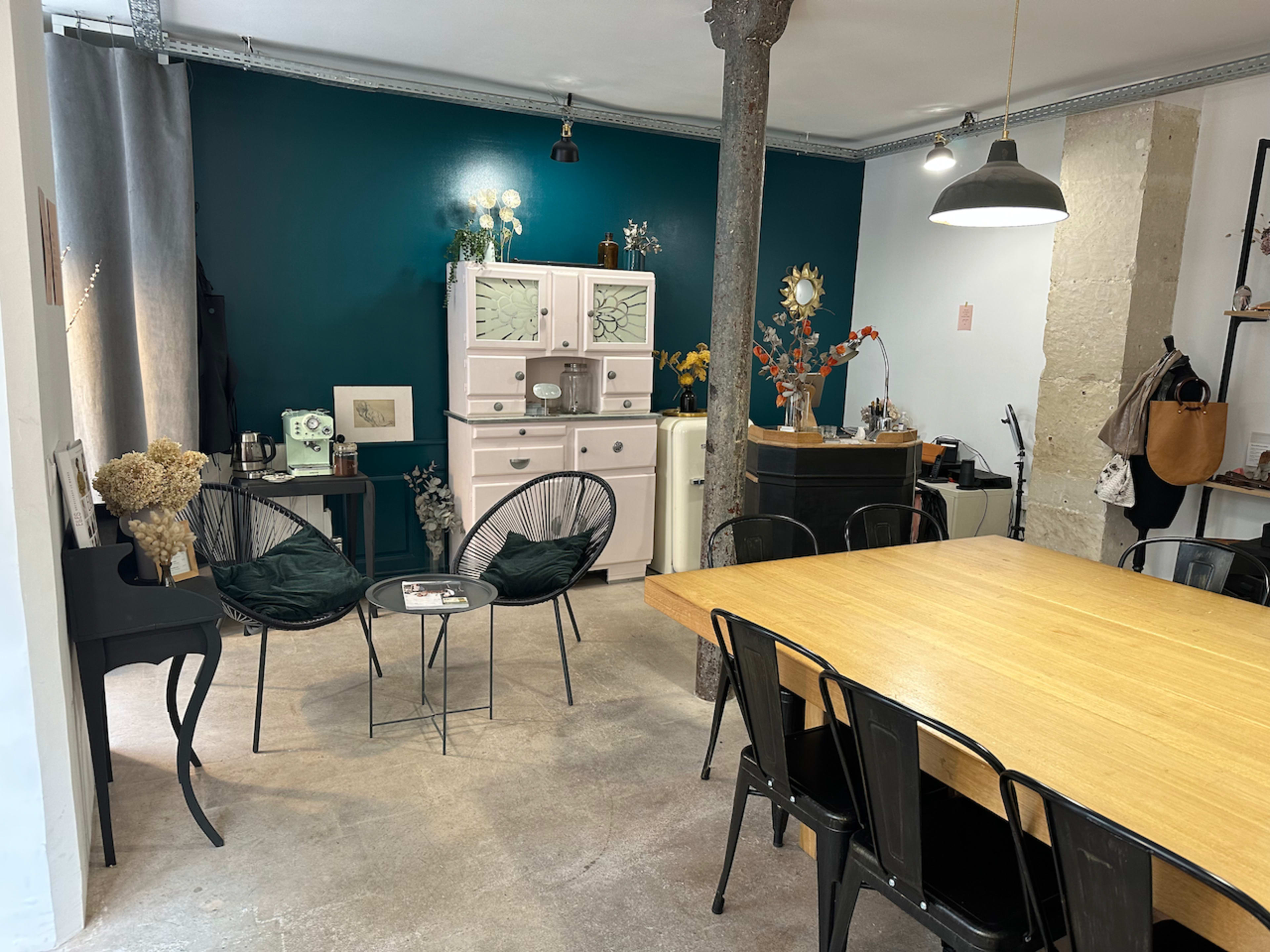 A cozy interior space features a wooden dining table, black chairs, and a mix of decorative items against a teal wall.