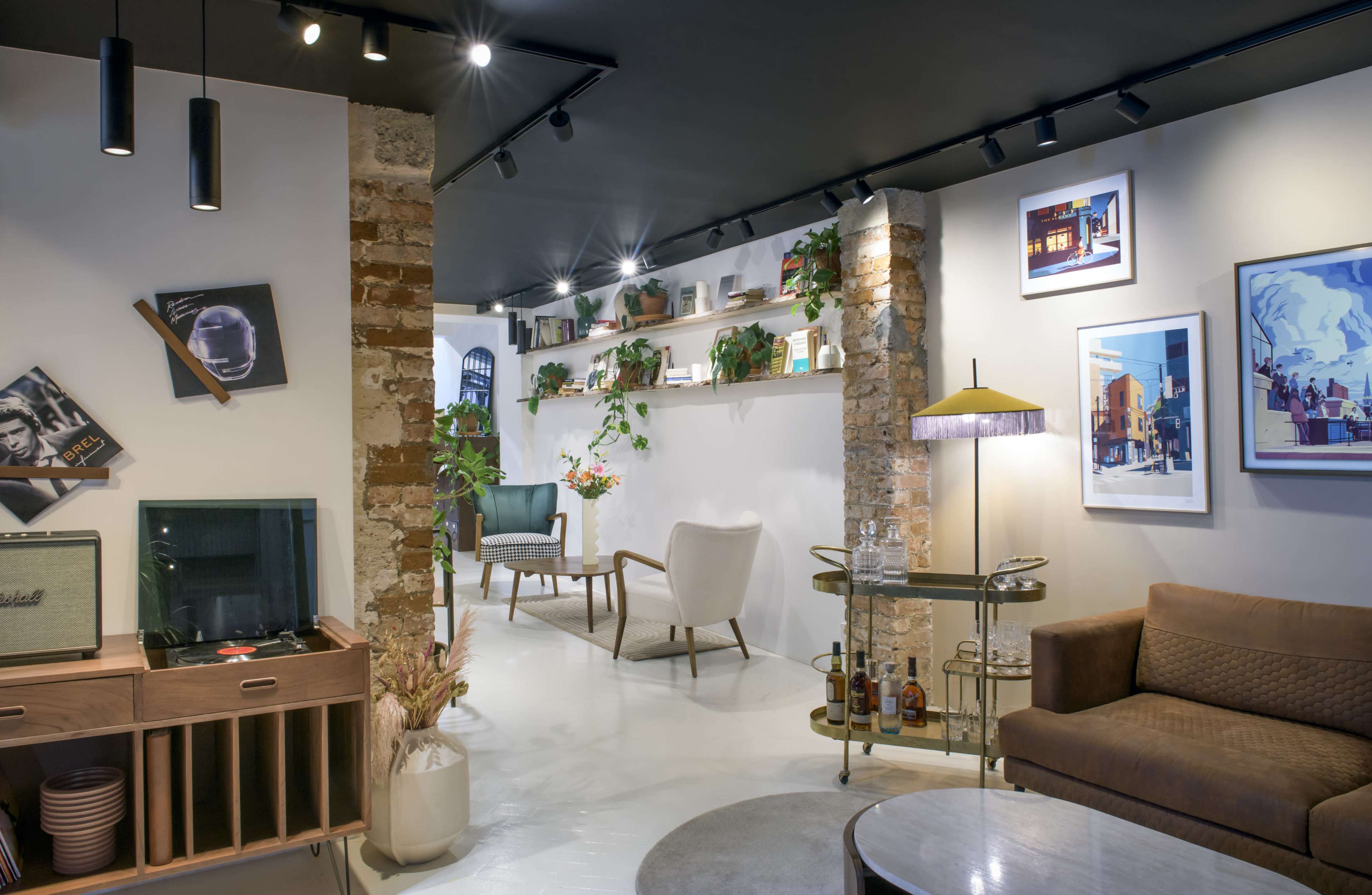 The image shows a modern interior space featuring a mix of vintage furniture, decorative plants, and framed artwork on the walls.