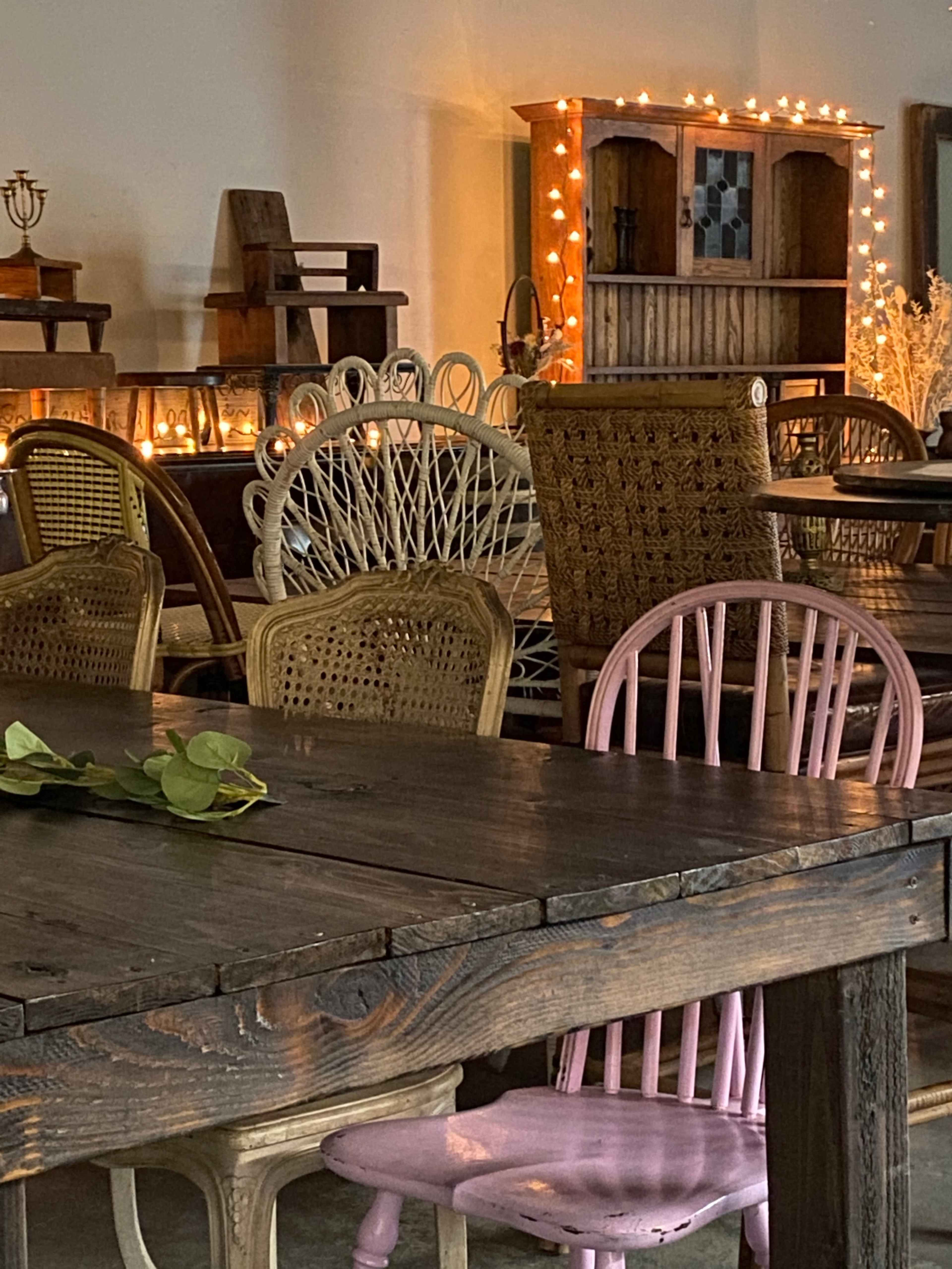 A collection of various chairs arranged around rustic wooden tables in a warmly lit café or event space.