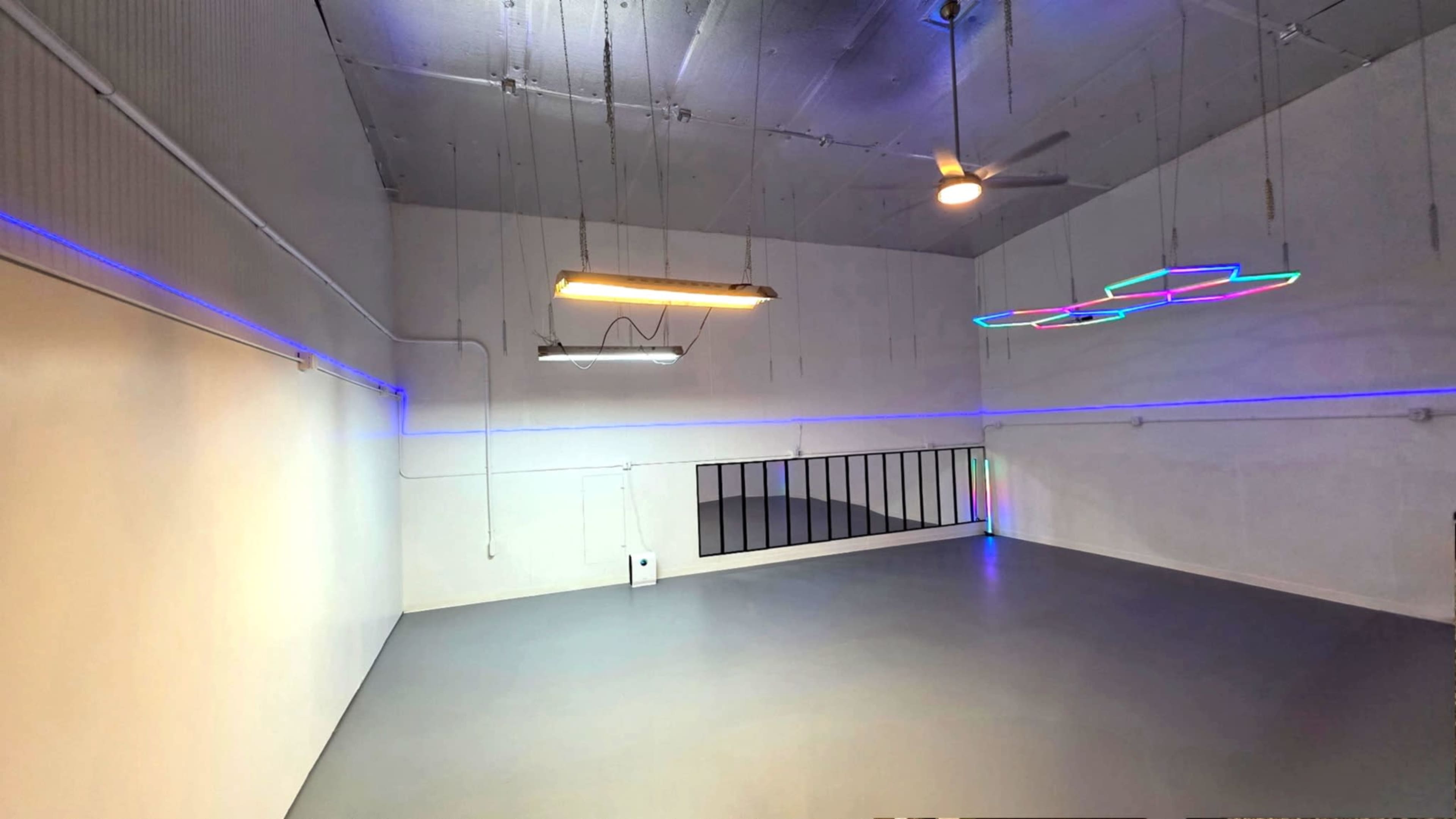 The image shows an empty studio space with gray flooring, white walls, and colorful LED light fixtures on the ceiling.