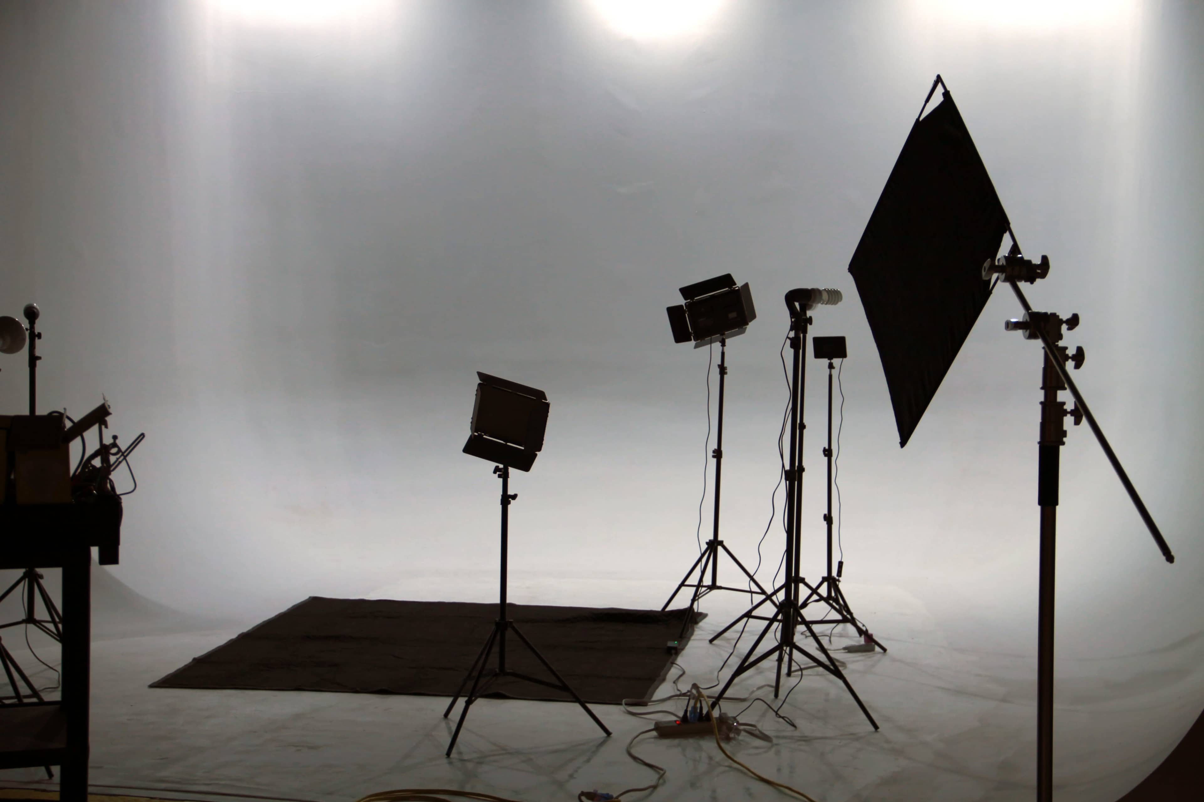 A photo studio setup with lighting equipment and a blank backdrop.