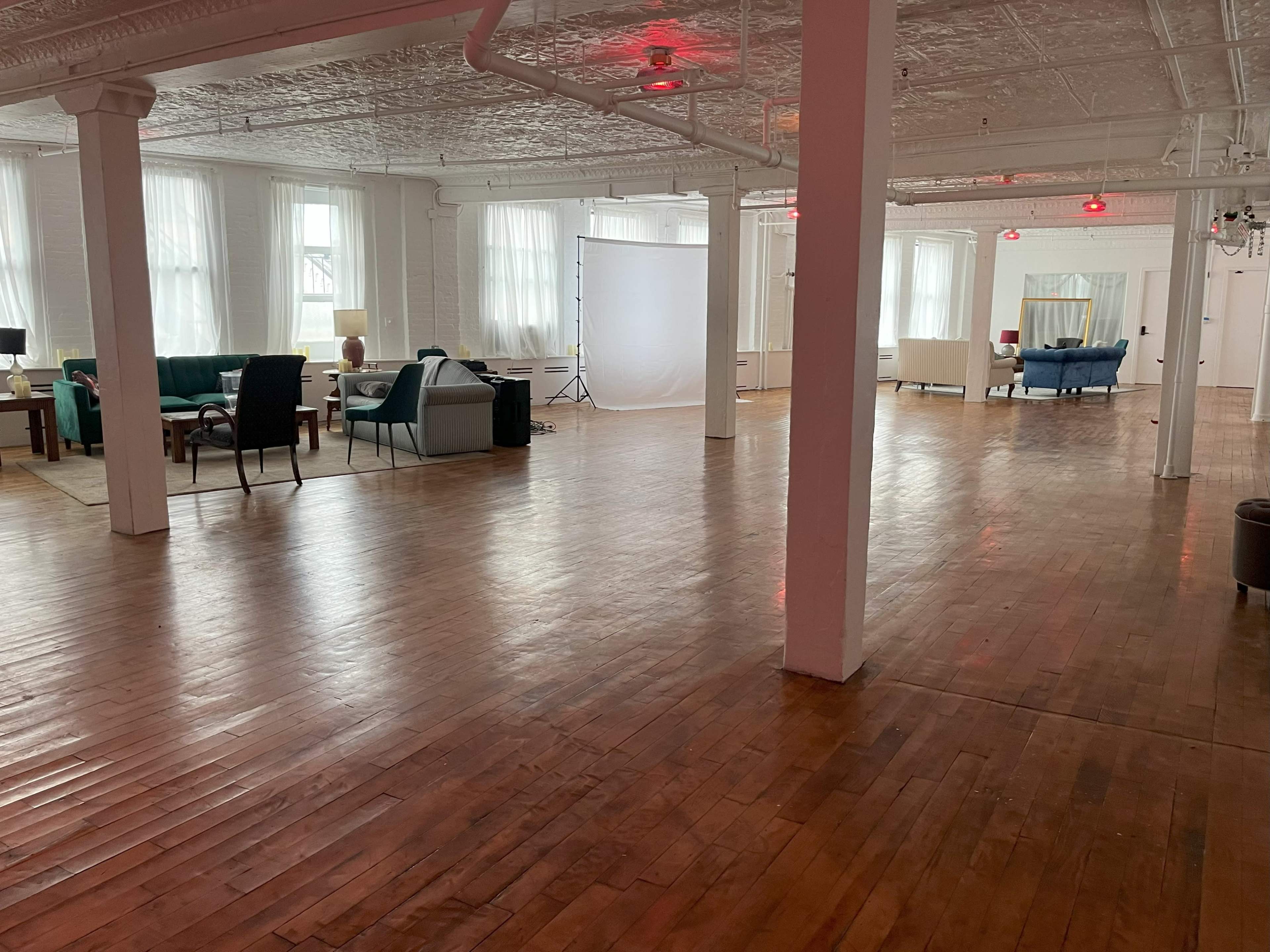 A spacious room with wooden floors, featuring various seating arrangements and bright natural light filtered through large windows.