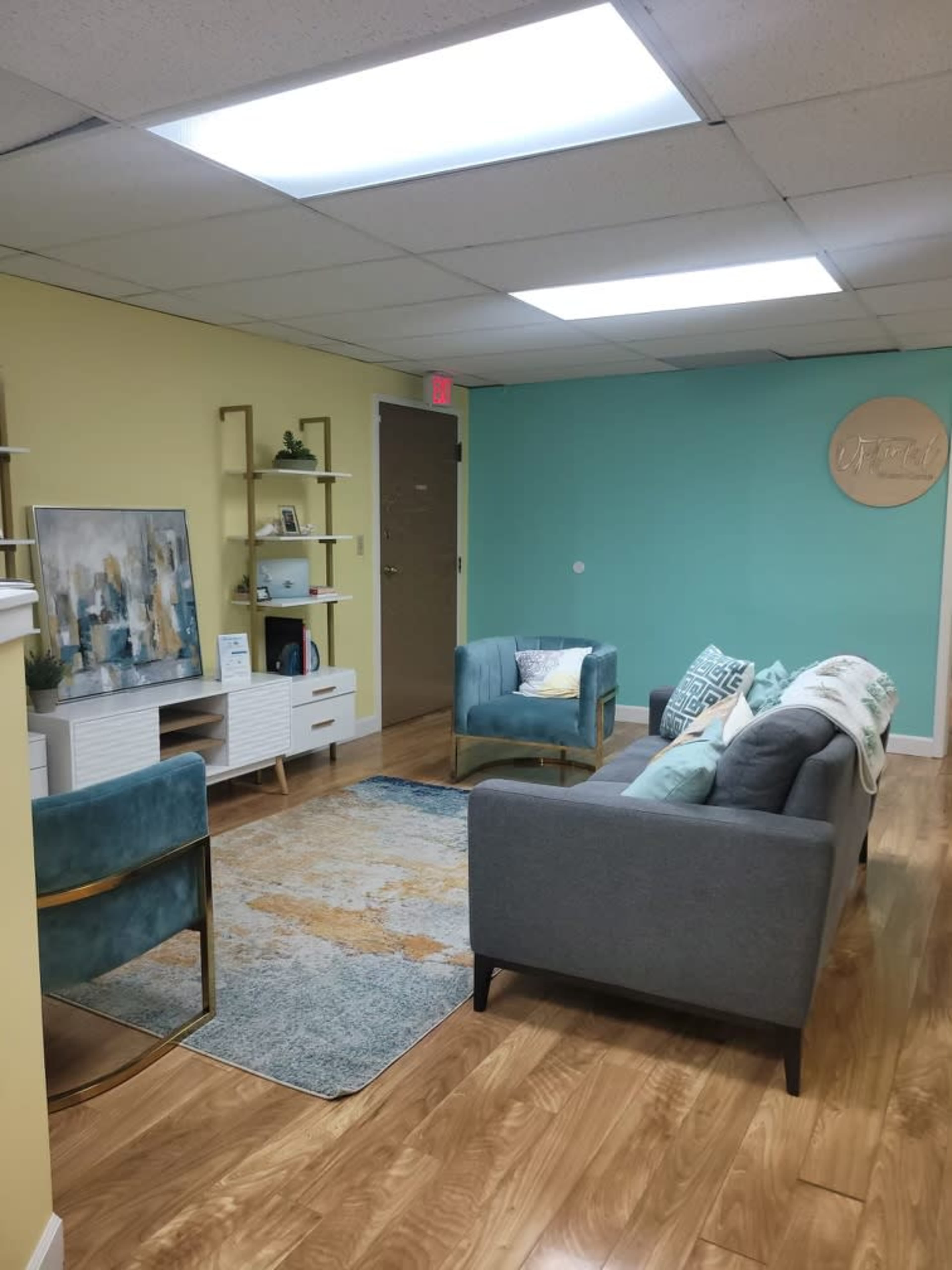 A modern waiting room with teal and yellow walls, wooden flooring, a rug, two sofas, and a decorative wall sign.