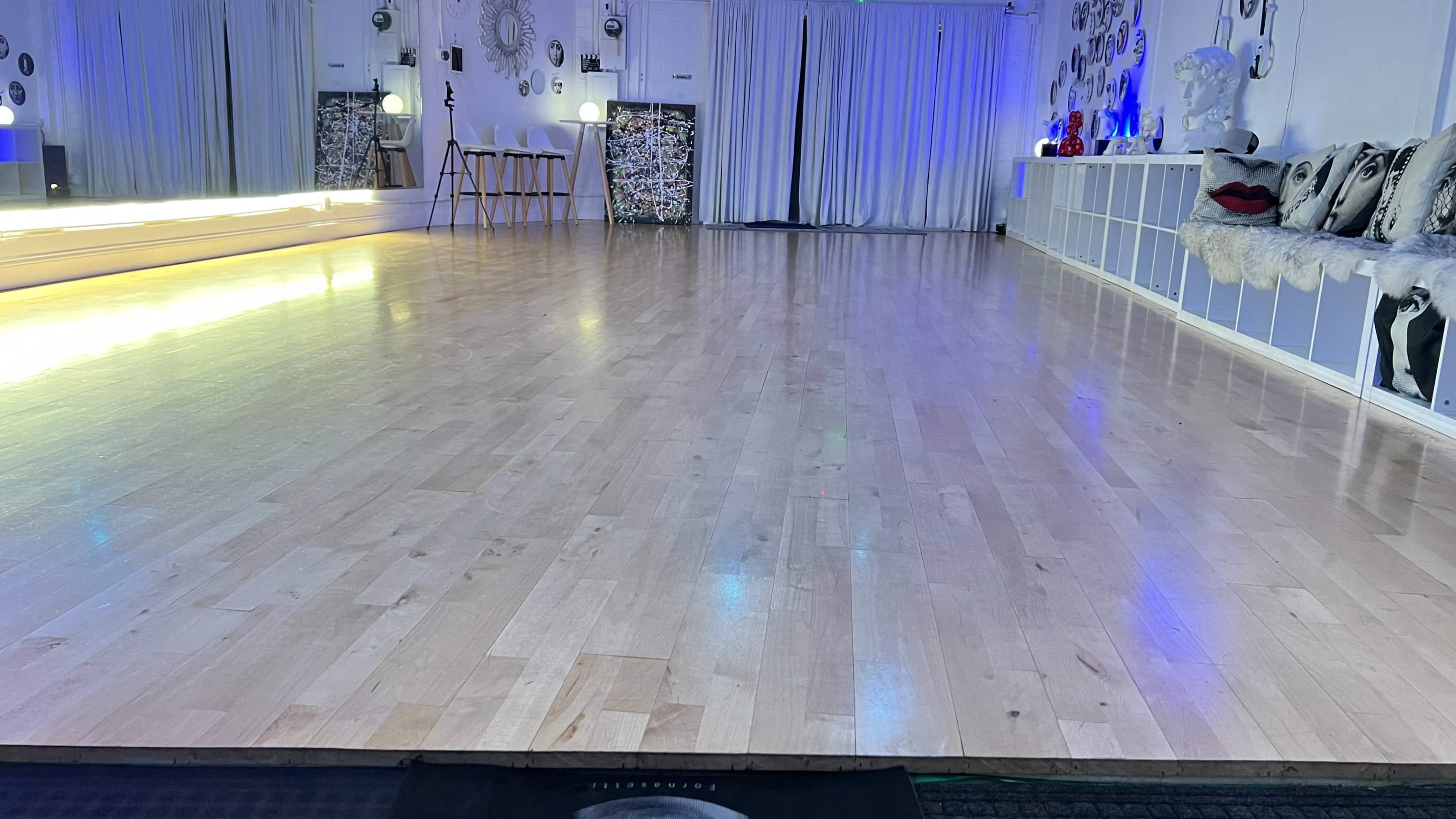 A spacious dance studio with a polished wooden floor, ambient lighting, and decorative wall elements.