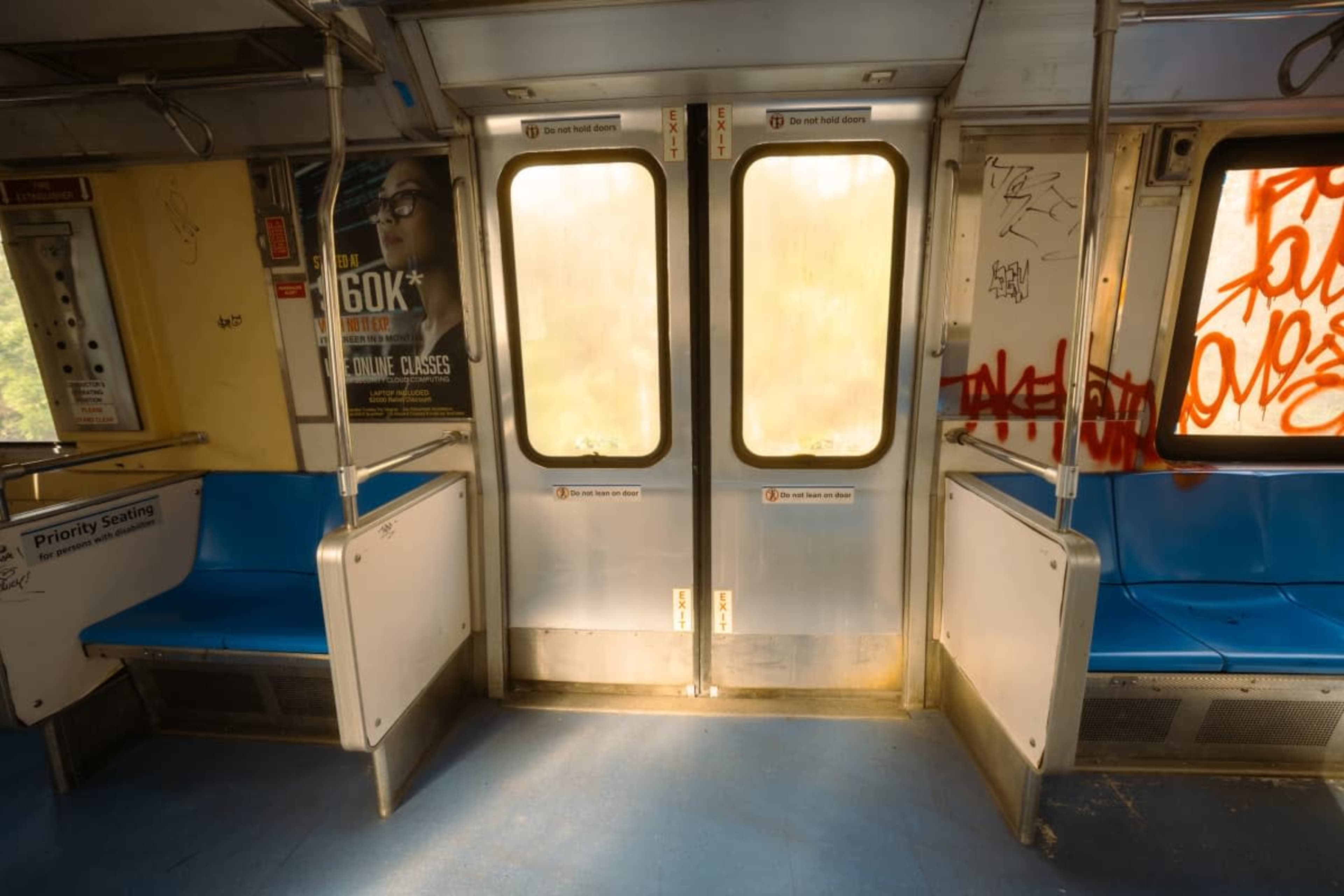 The image shows the interior of a subway car featuring empty blue seats and doors covered with graffiti.