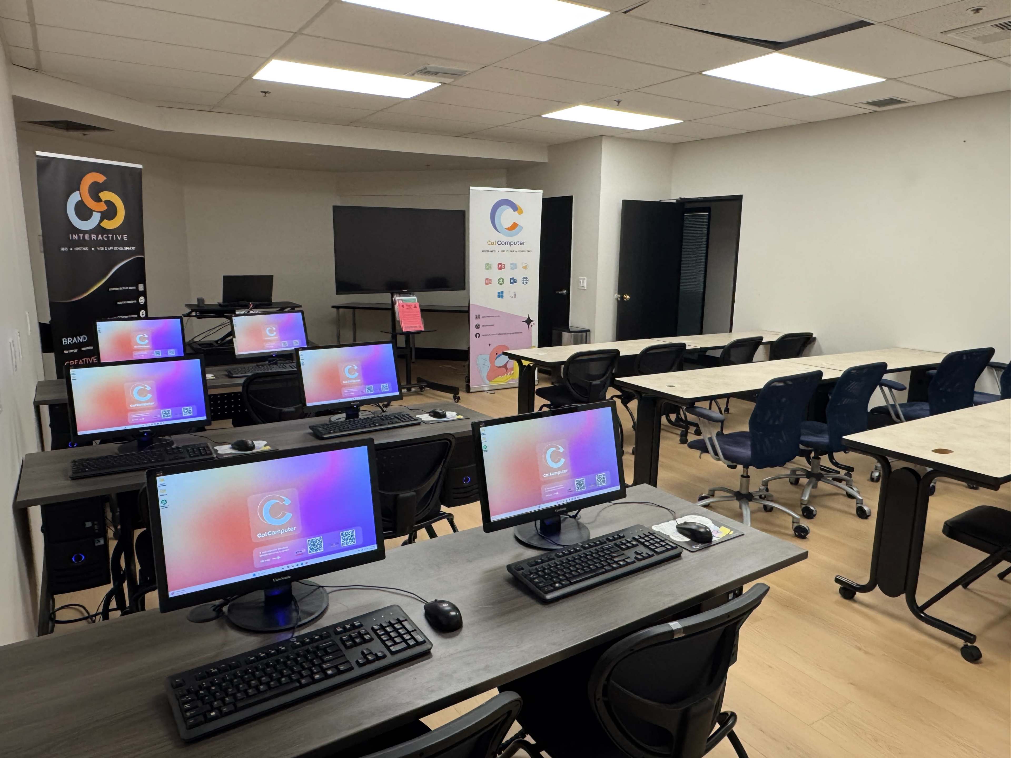 A classroom with multiple computer stations, each equipped with monitors, and additional tables and chairs arranged for instruction.