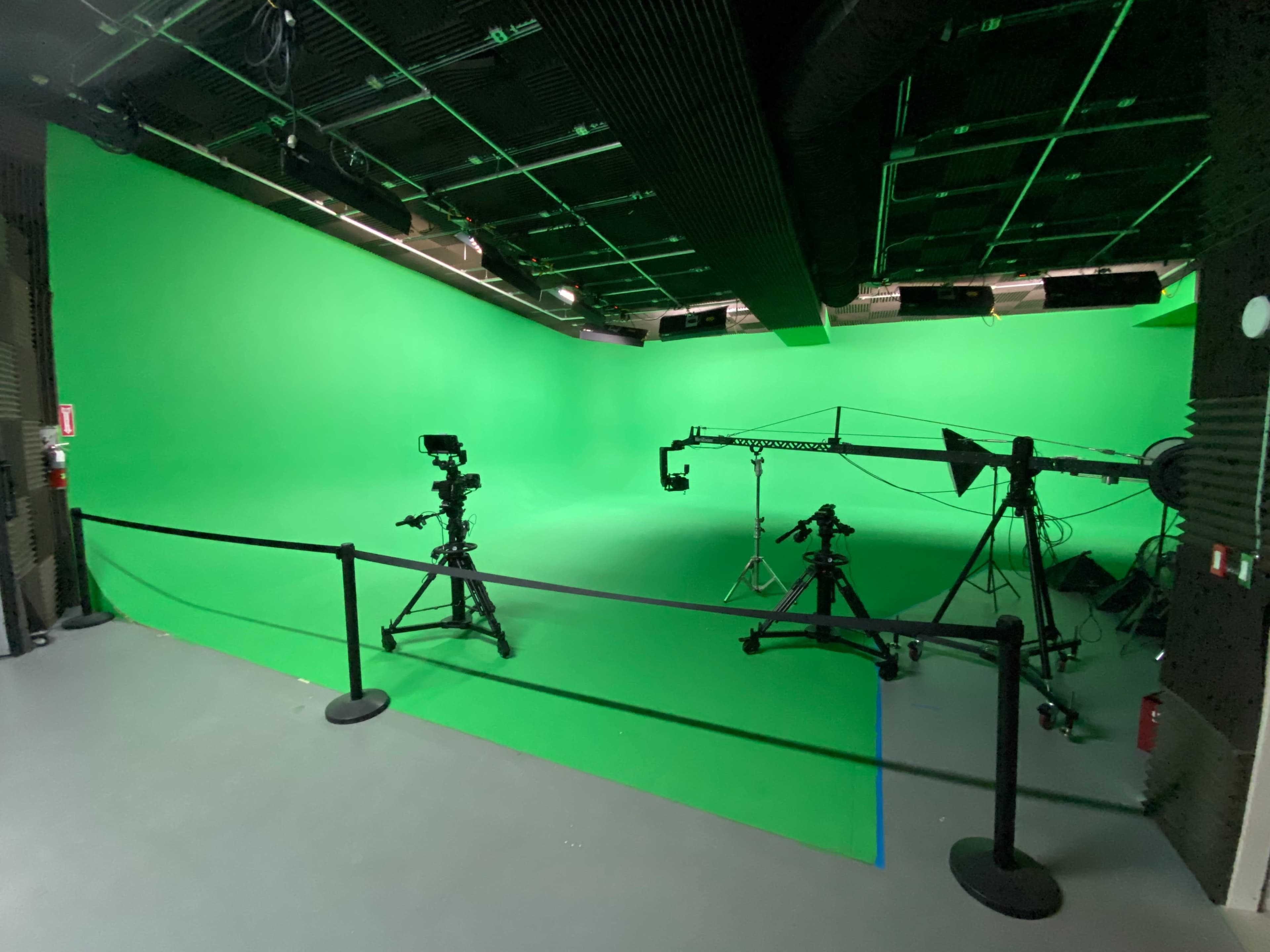 A green-screen studio equipped with multiple camera setups and a ceiling-mounted camera crane.