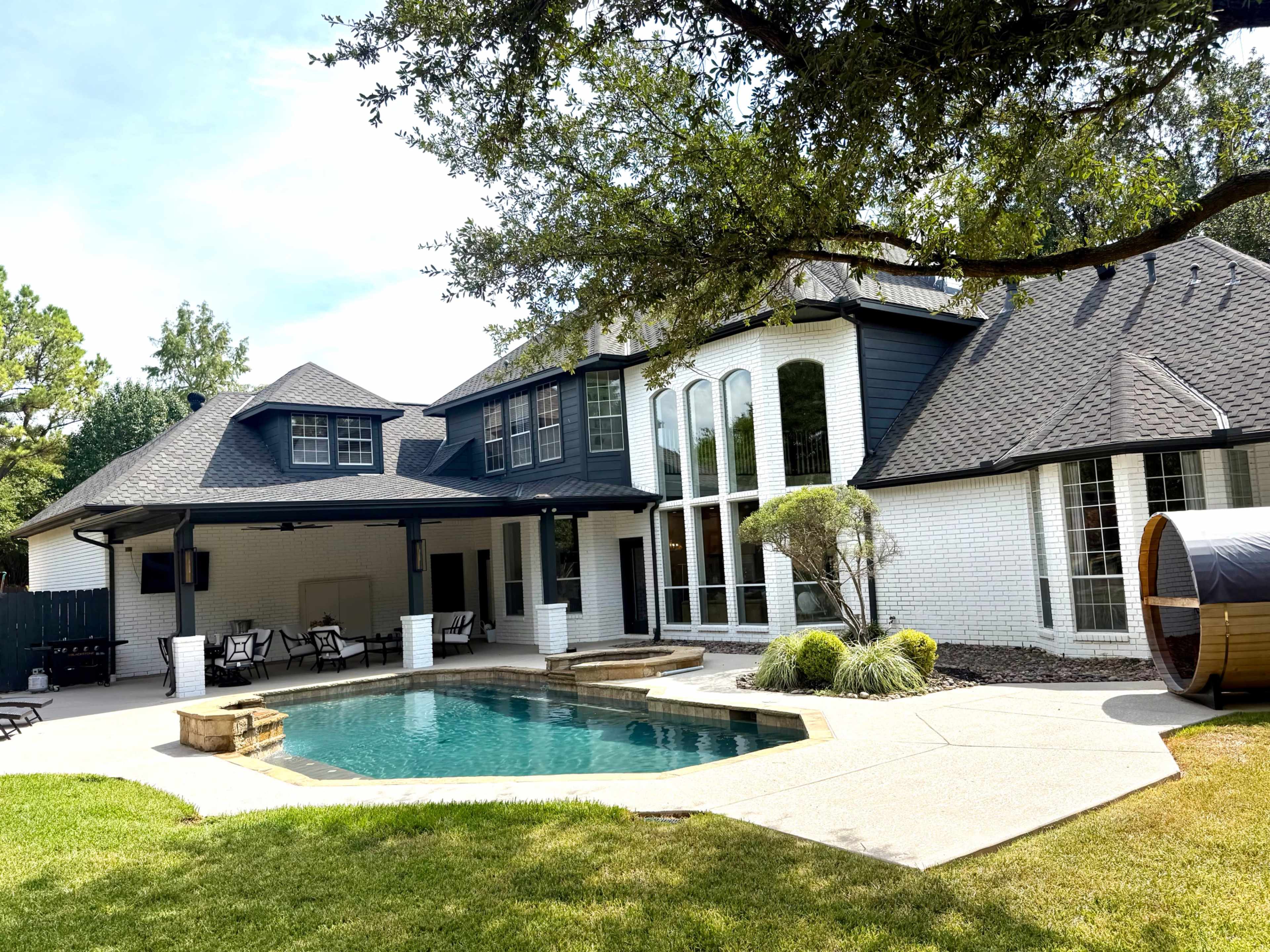 The image shows a modern two-story house with a swimming pool and outdoor seating area, surrounded by lush greenery.