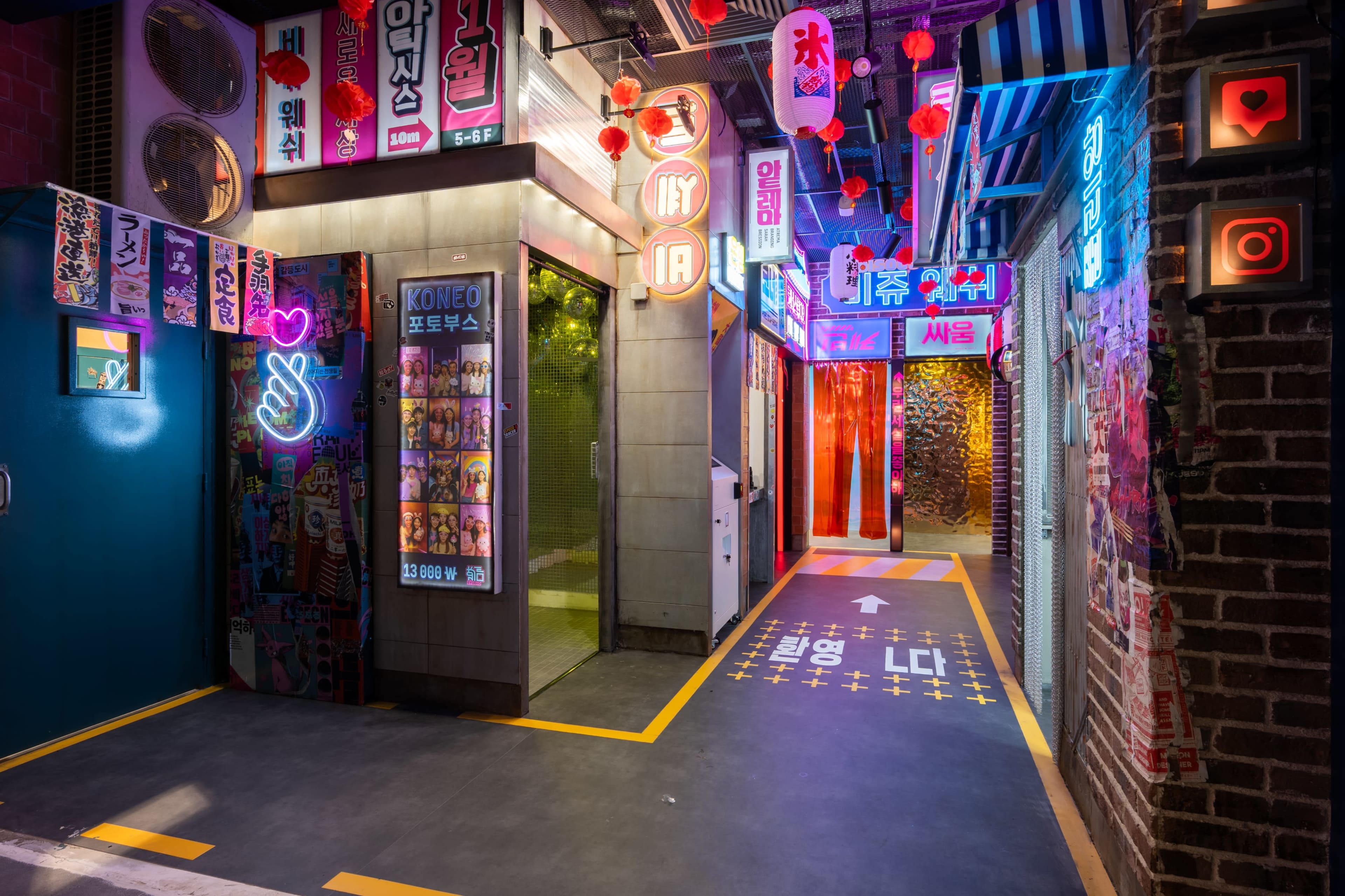 The image shows a vibrant commercial alleyway illuminated by neon signs and lanterns, featuring storefronts with various graphics and colorful lighting.