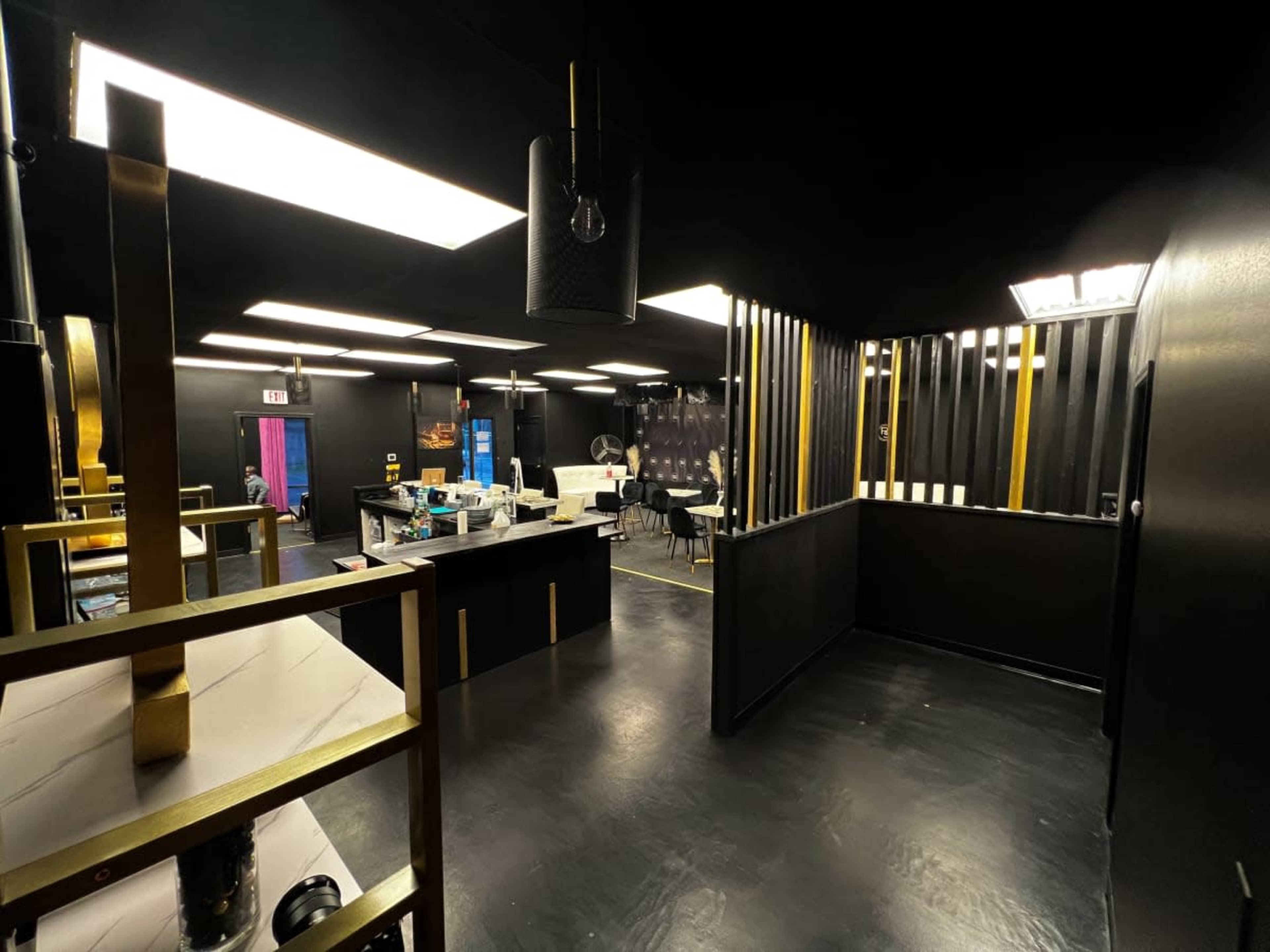 A modern interior space with black walls, gold accents, and various furniture arrangements, including a reception area and seating.
