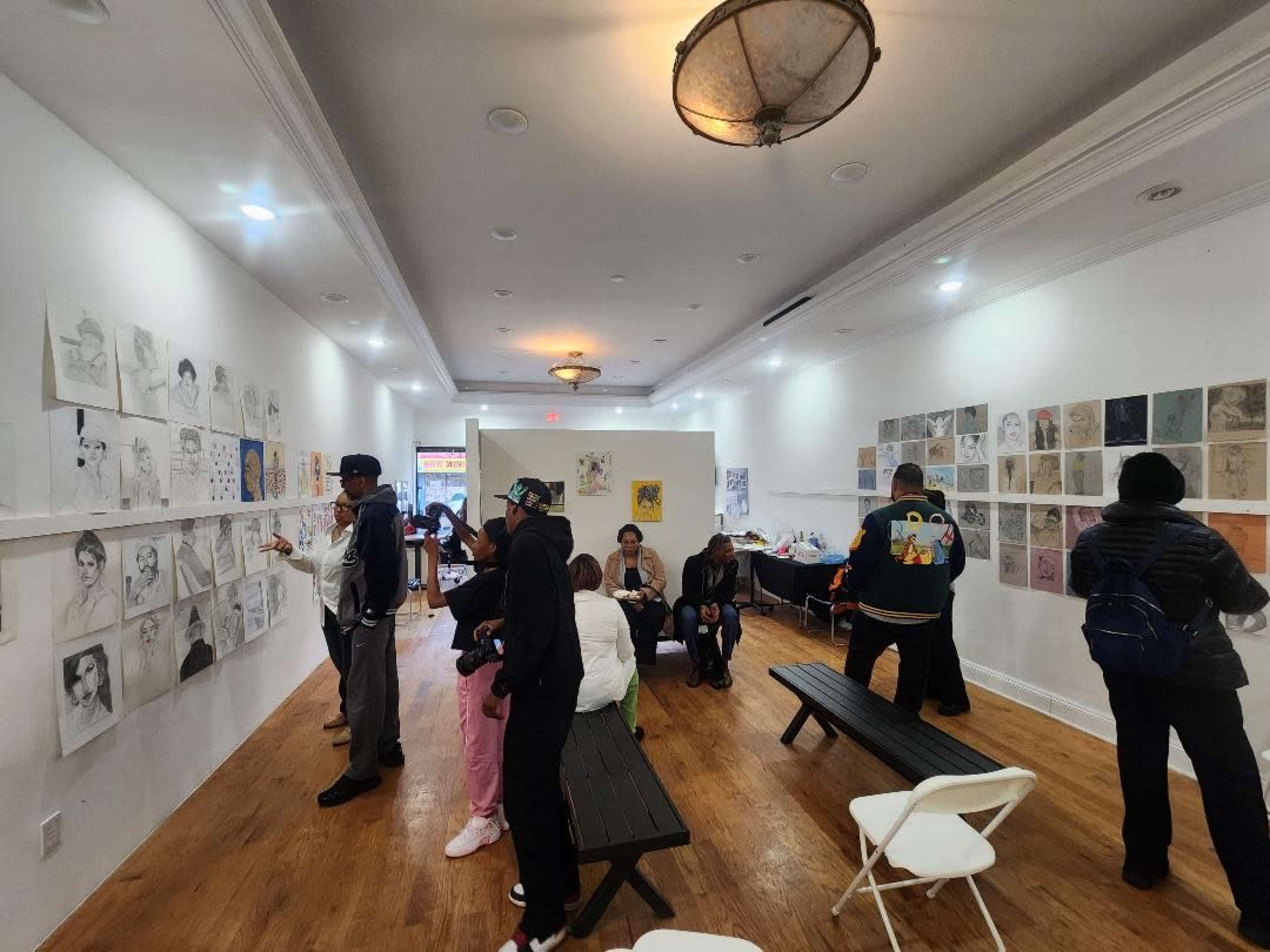 People are observing and discussing drawings displayed on the walls of an art gallery featuring a light-filled, spacious interior.