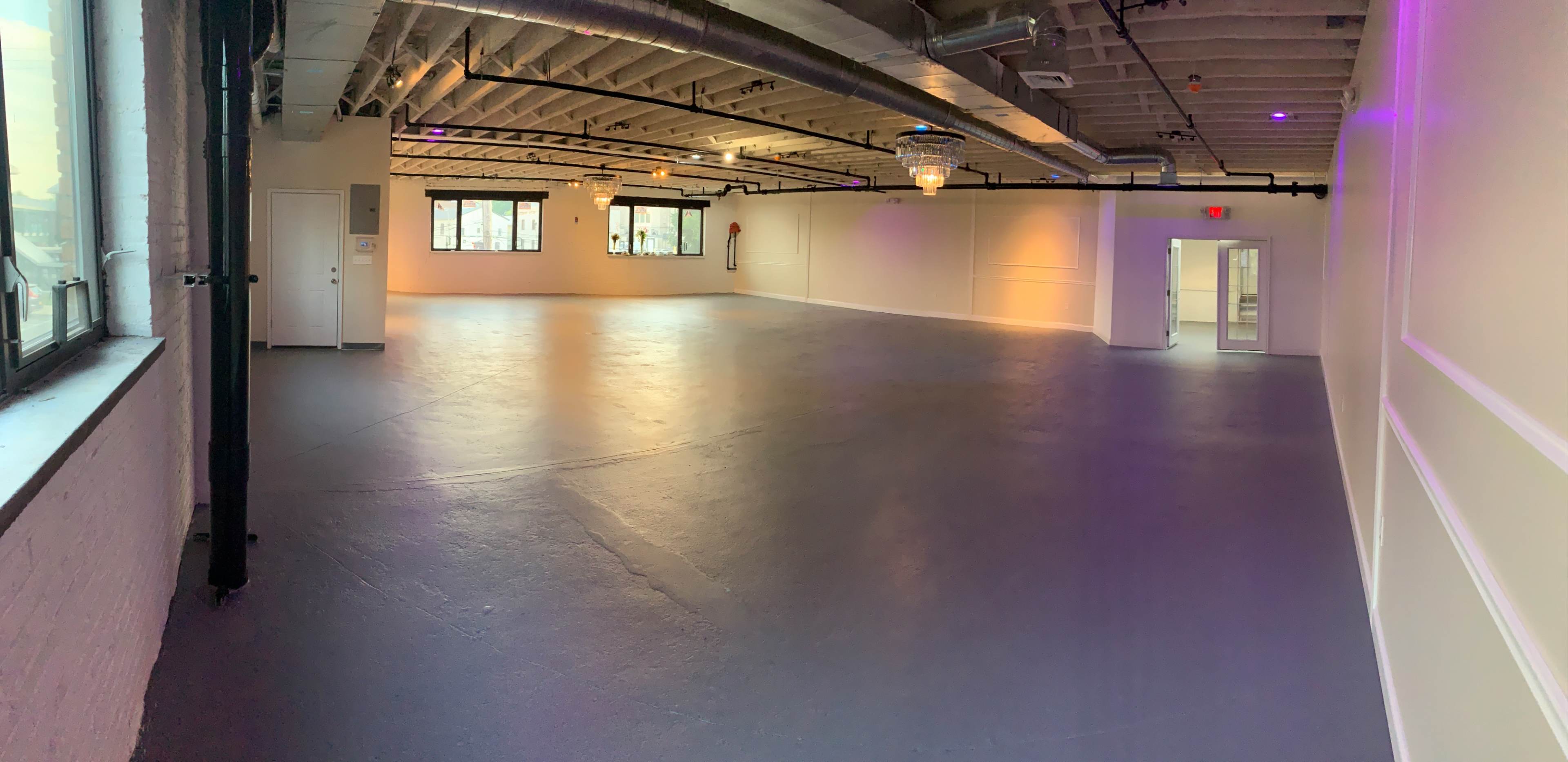 A spacious, empty room with large windows, fluorescent lighting, and a smooth concrete floor.