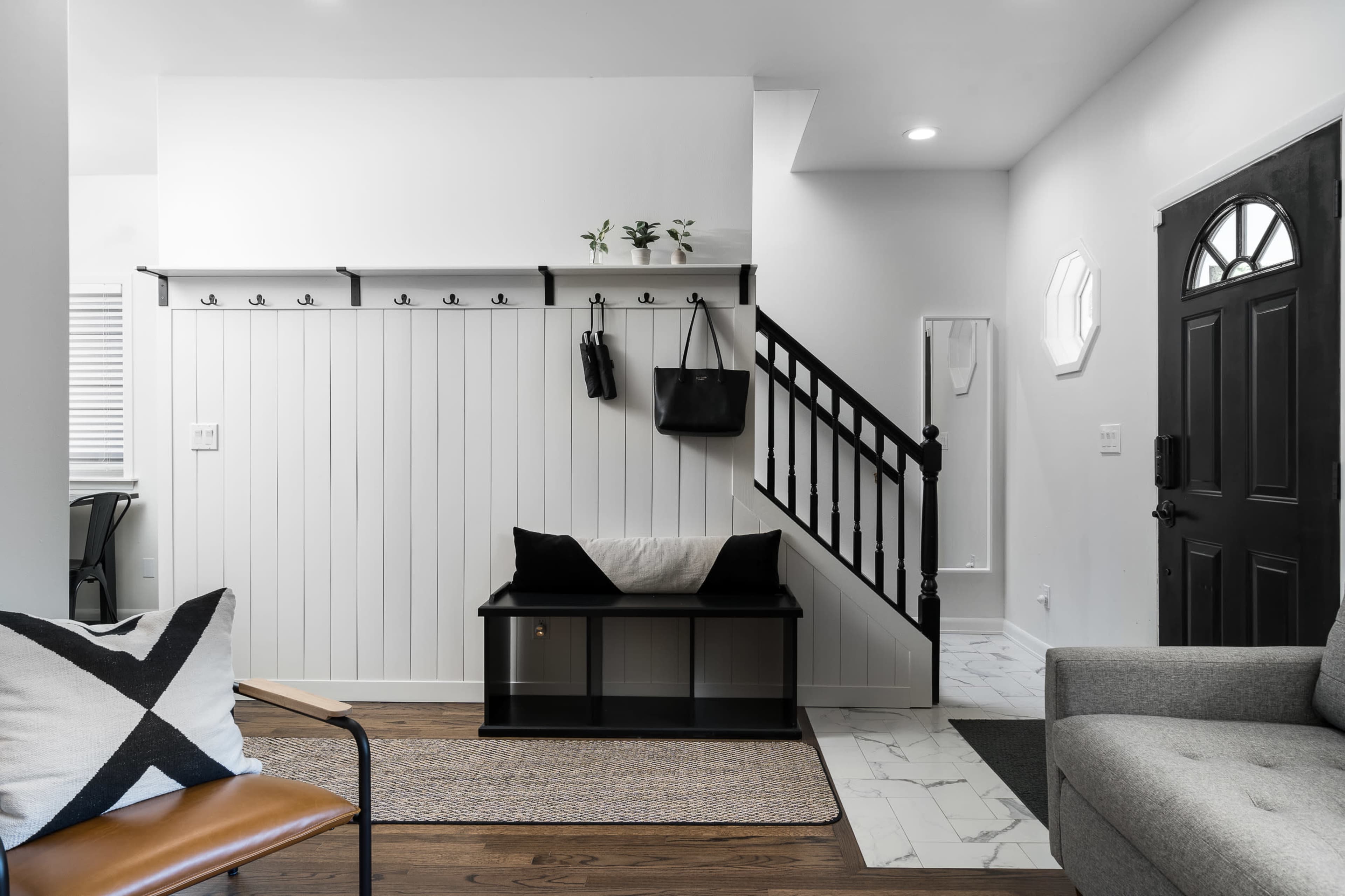 A modern entryway with a white walled coat rack, a dark staircase, a black front door, and a gray sofa.