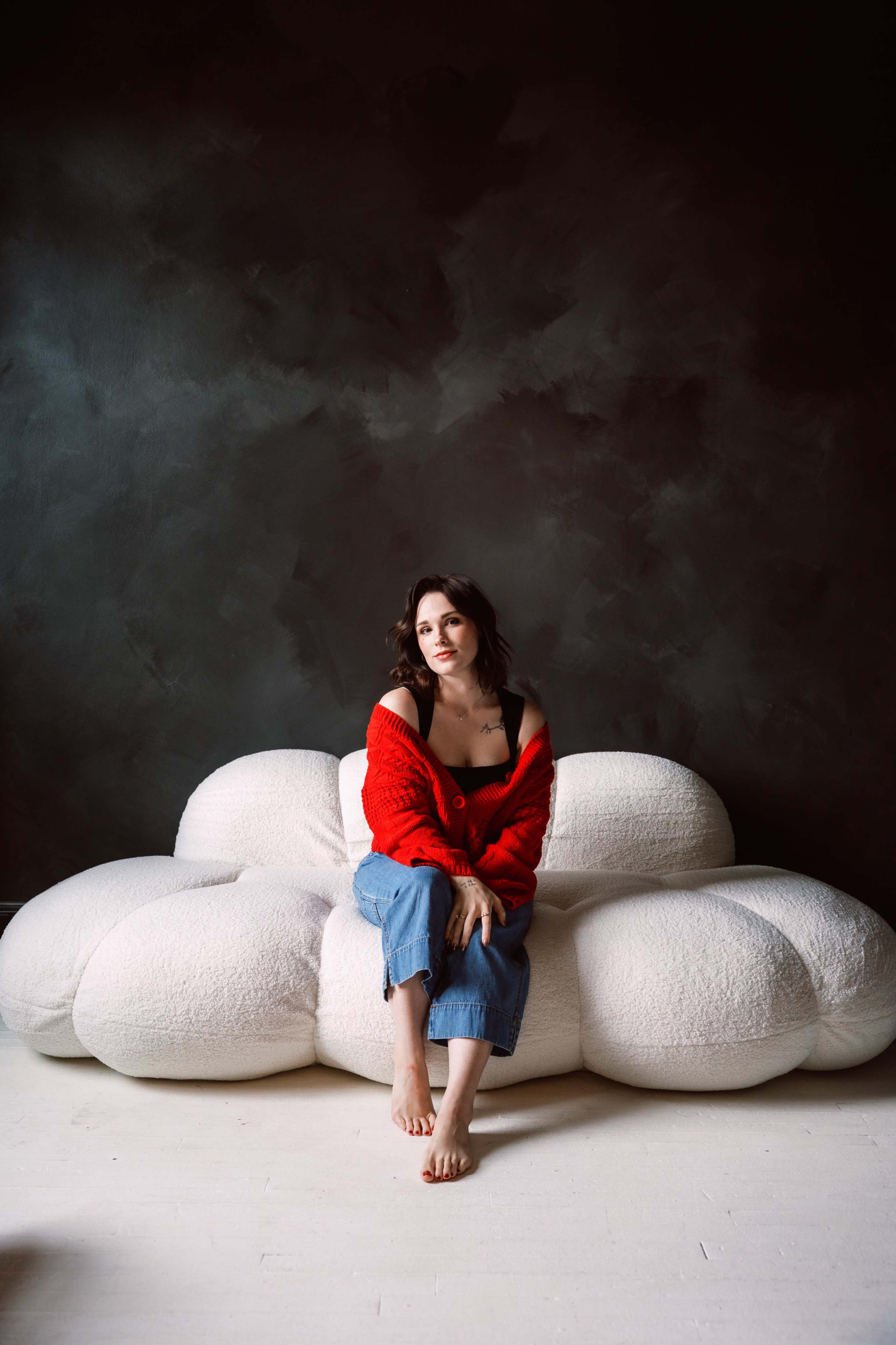 A person sits on a large, cloud-shaped white sofa against a dark wall.