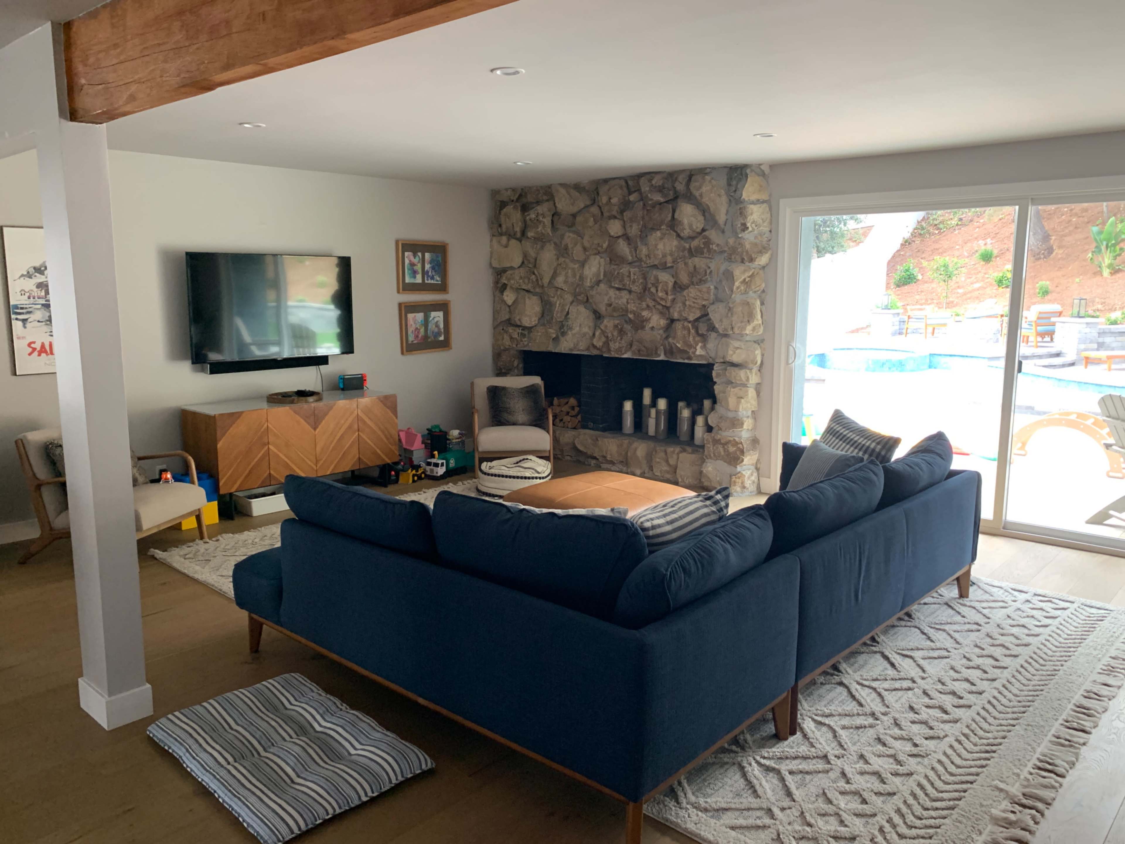The living room features a blue sectional sofa, a stone fireplace, a television mounted on the wall, and a view of a pool area through sliding glass doors.
