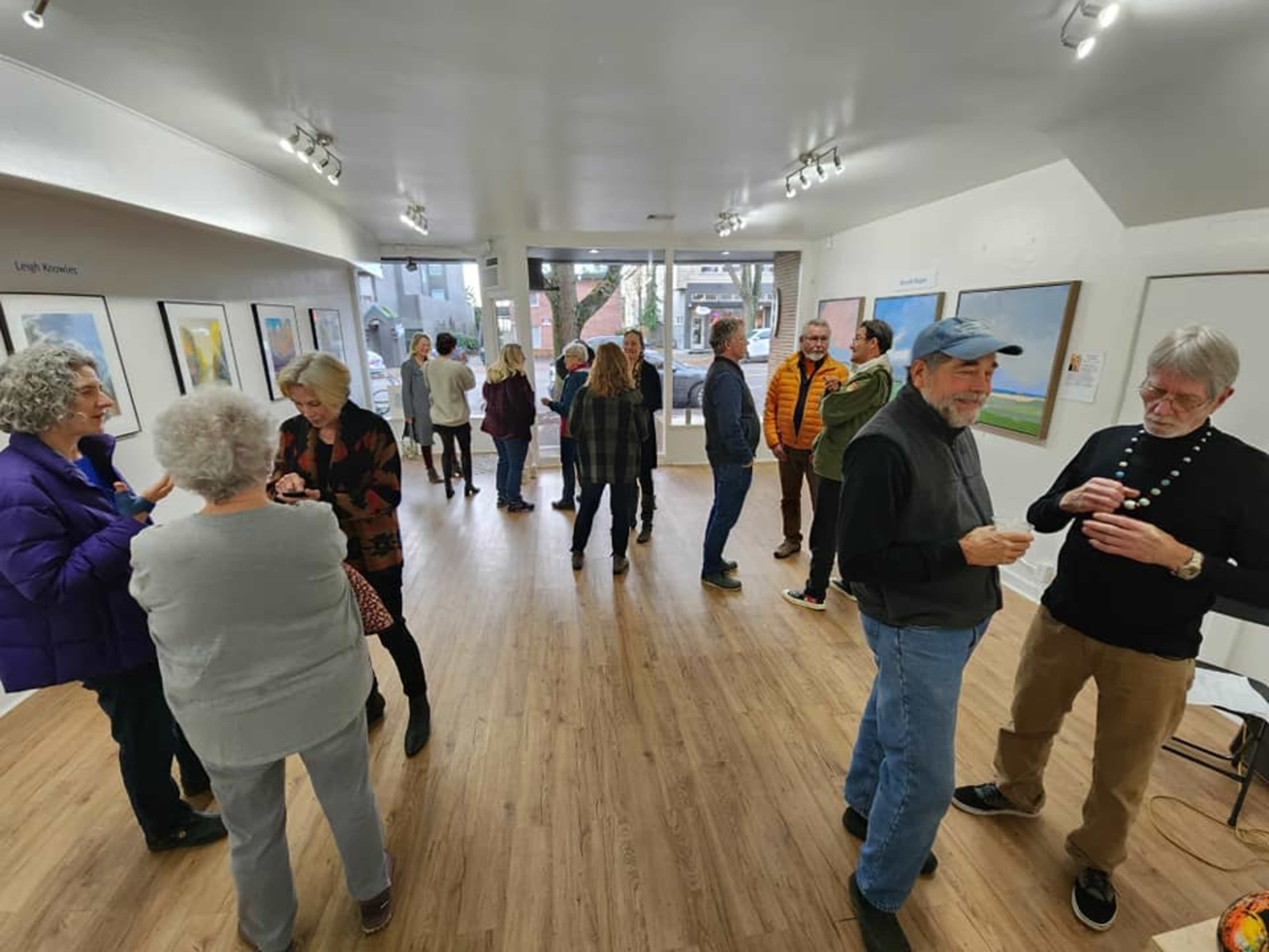 A group of people interacts in an art gallery featuring various framed artworks on the walls.
