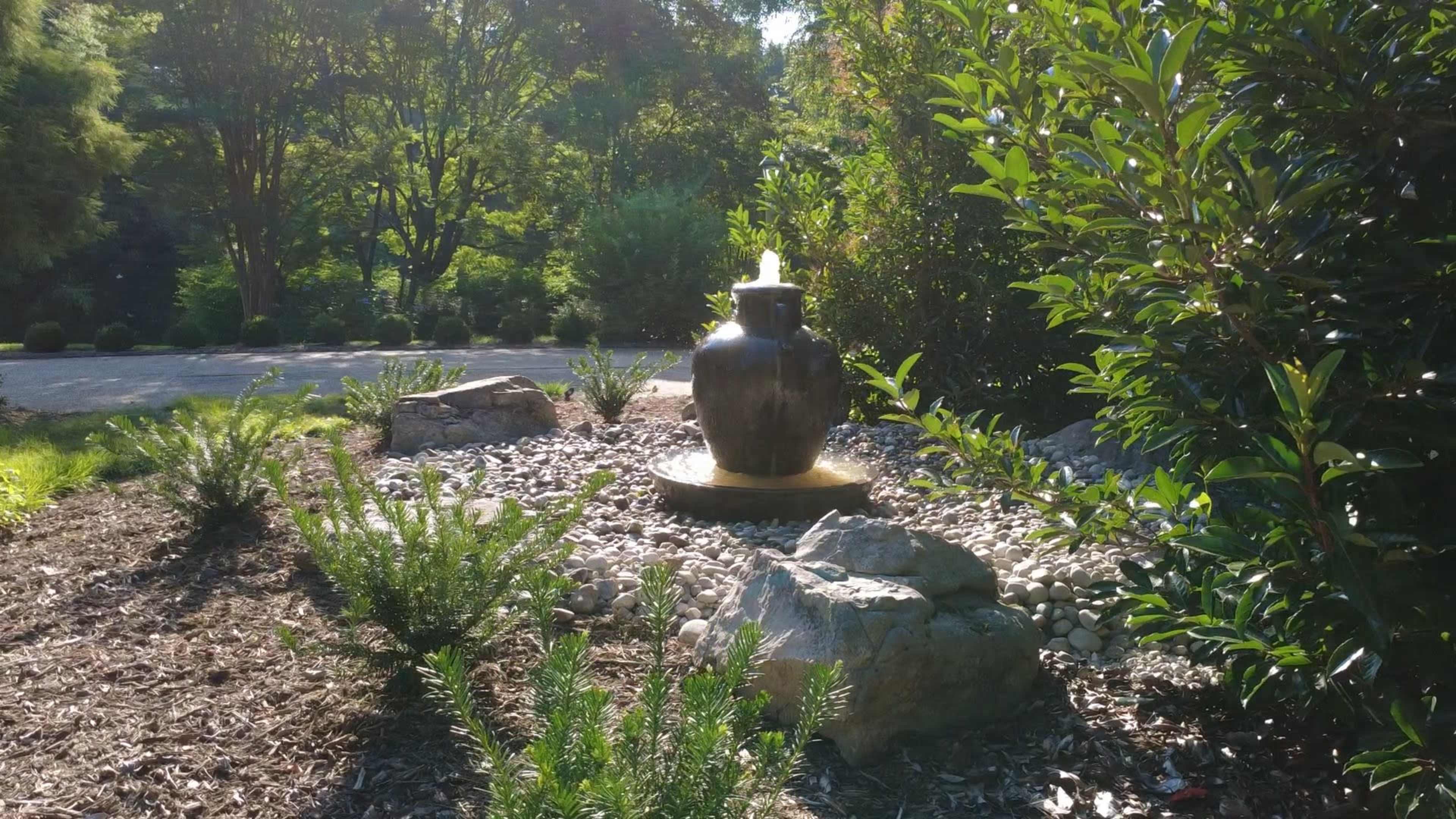 A decorative water fountain stands among rocks and greenery in a landscaped garden.